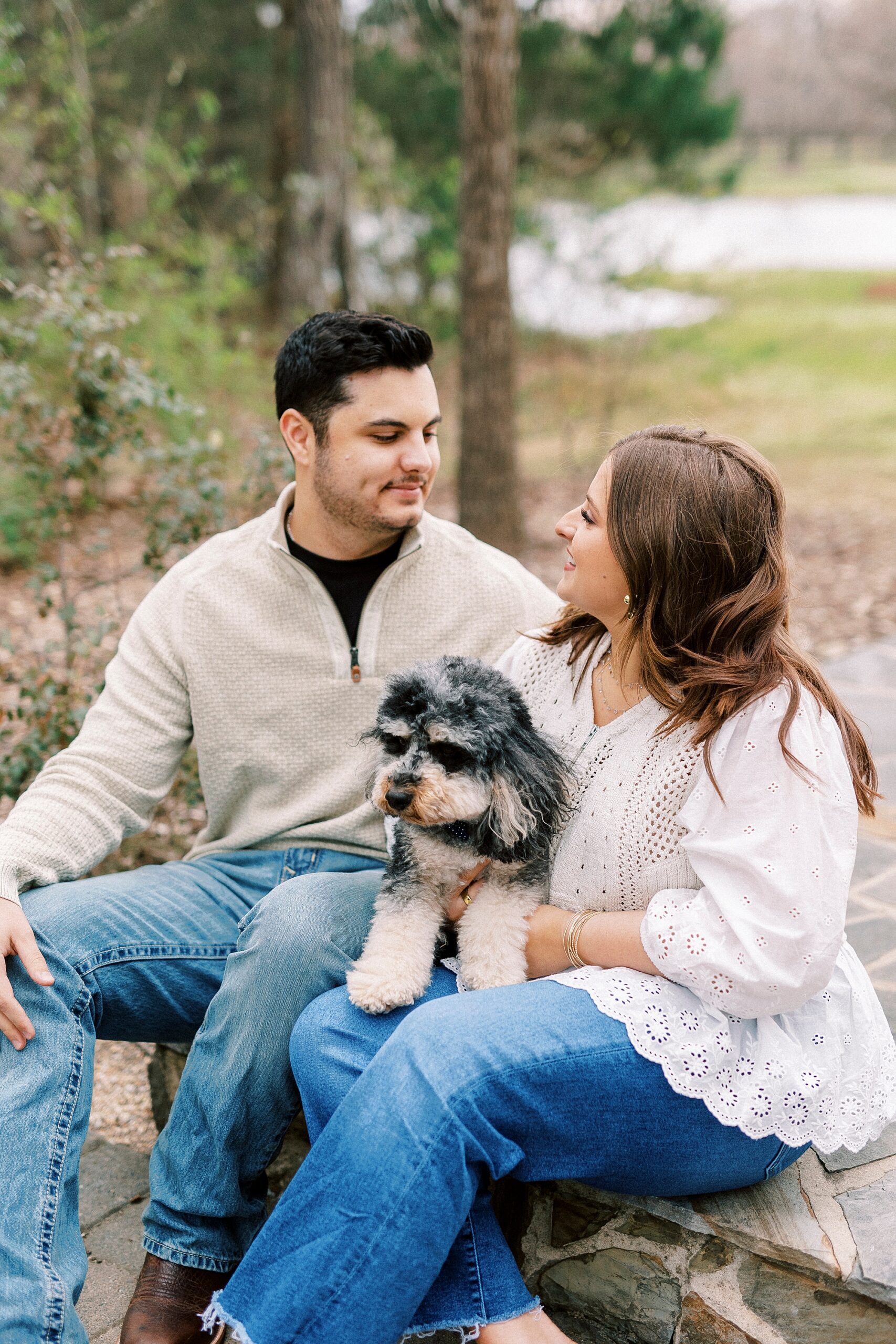 man and woman sit together with dog between them during engagement session at Morning Glory Farm