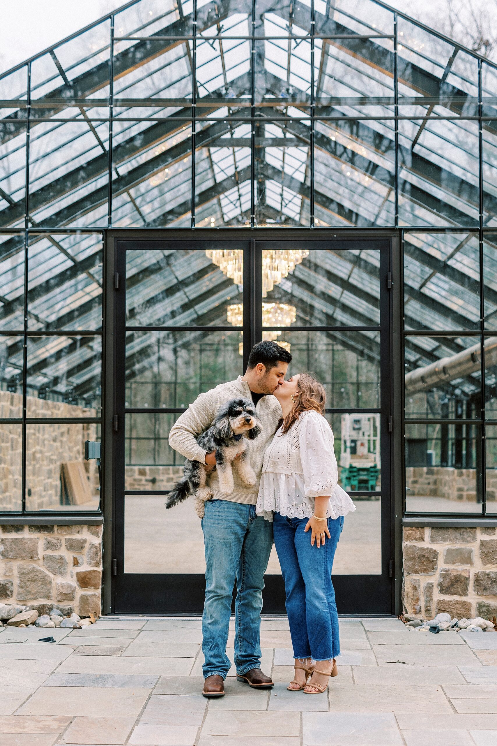 engaged couple kisses outside glass building at Morning Glory Farm