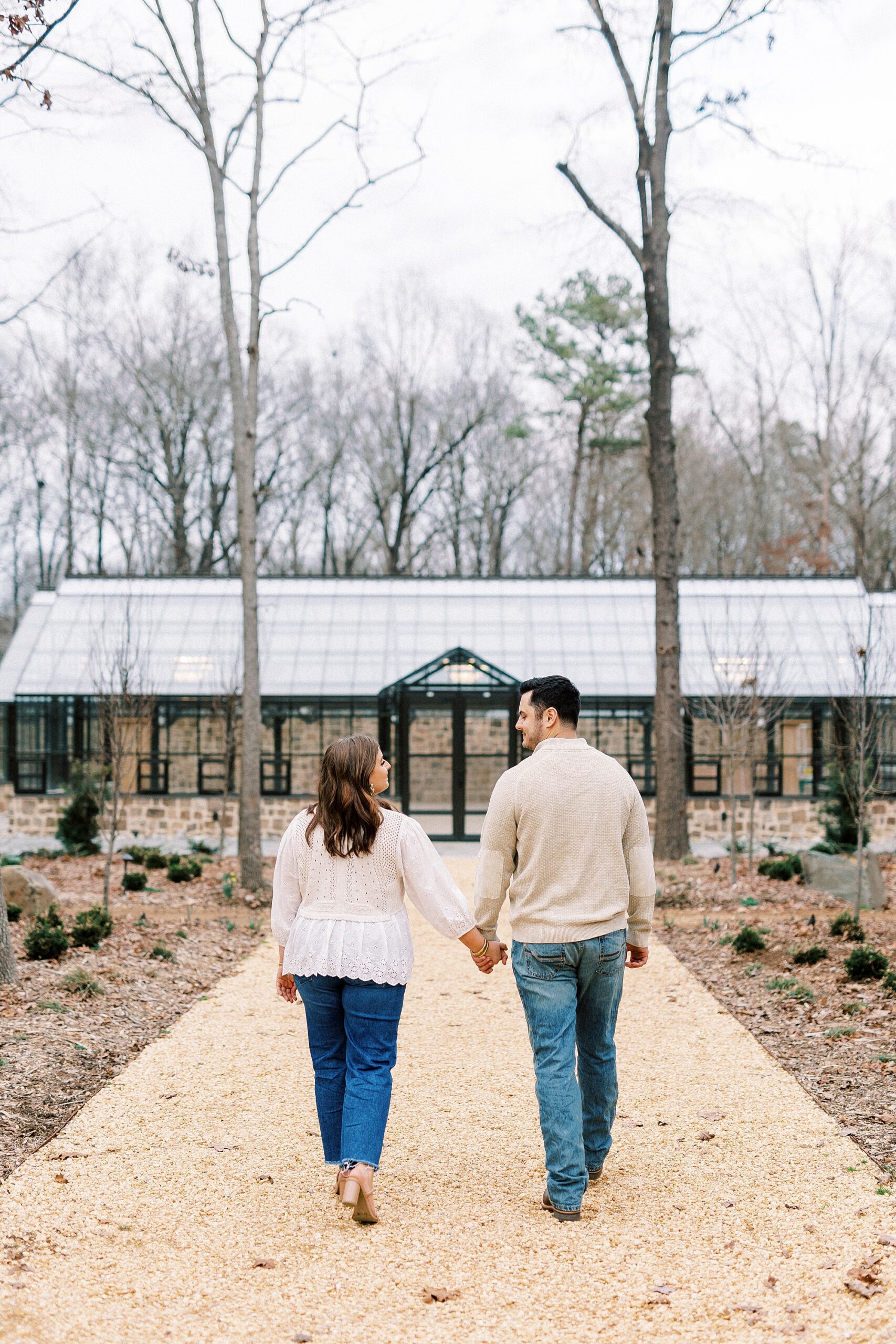 couple holds hands walking towards glass building at Morning Glory Farm