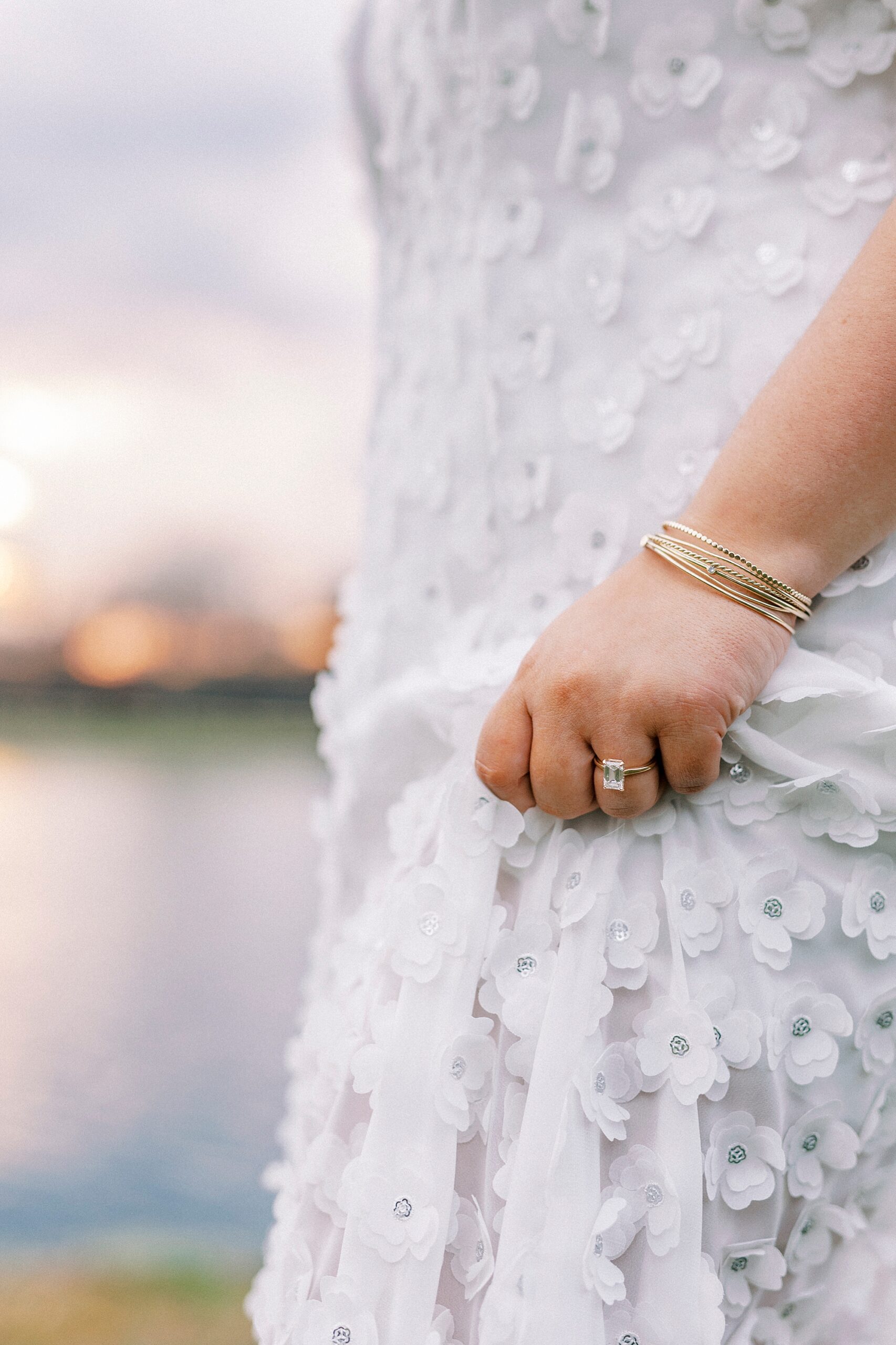 woman holds skirt of white dress showing off engagement ring