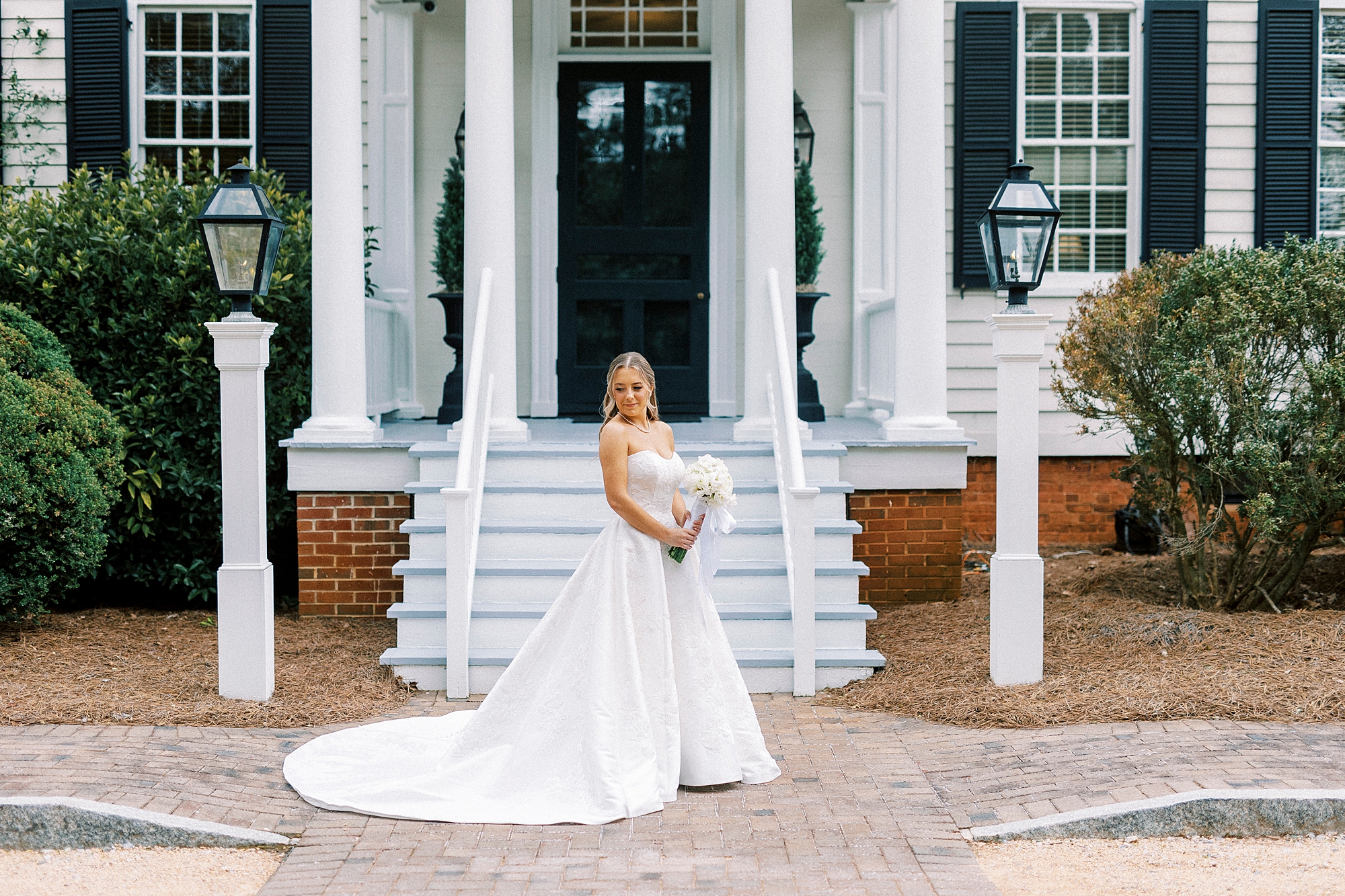 bride holds bouquet of white flowers outside front steps of the Sutherland in Wake Forest NC