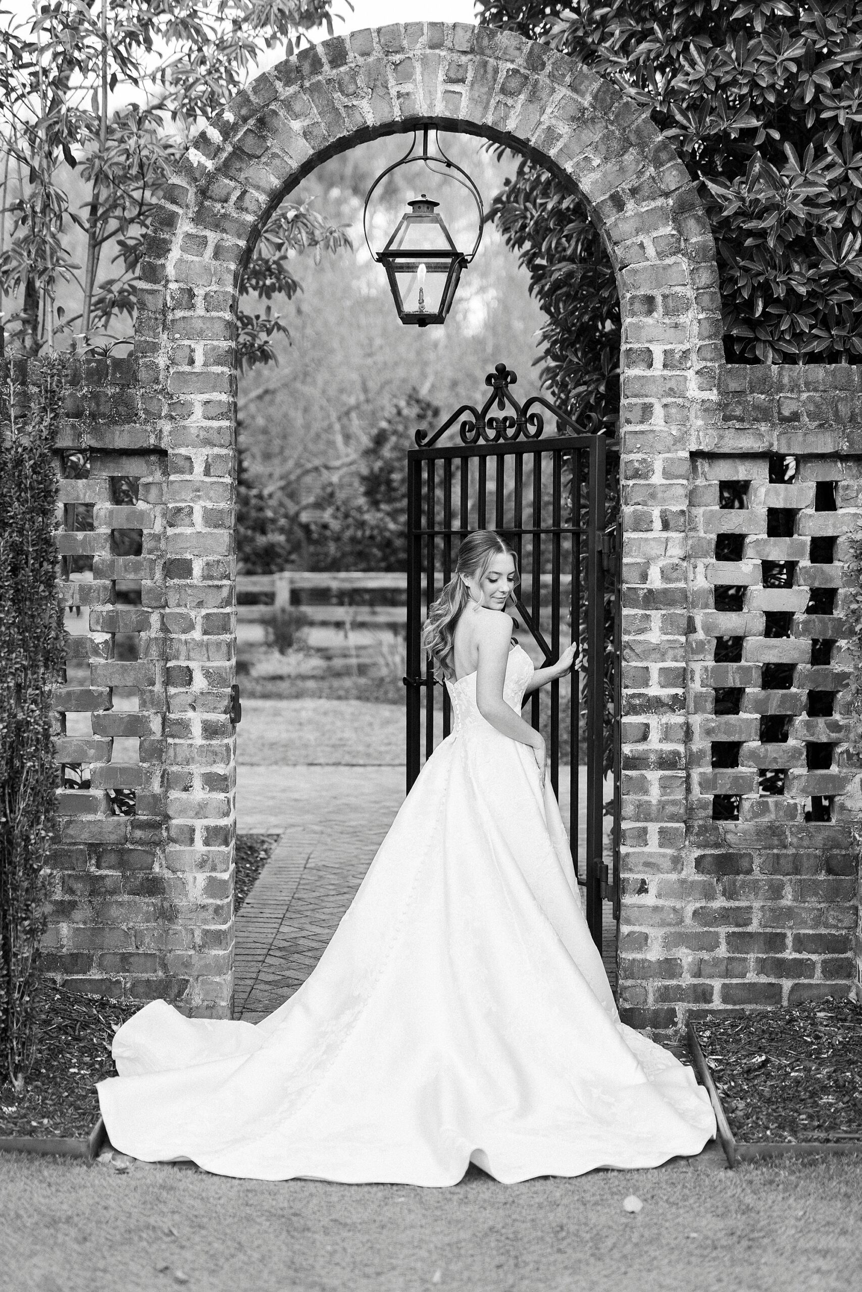 bride stands facing brick archway looking over shoulder during bridal portraits in Wake Forest NC
