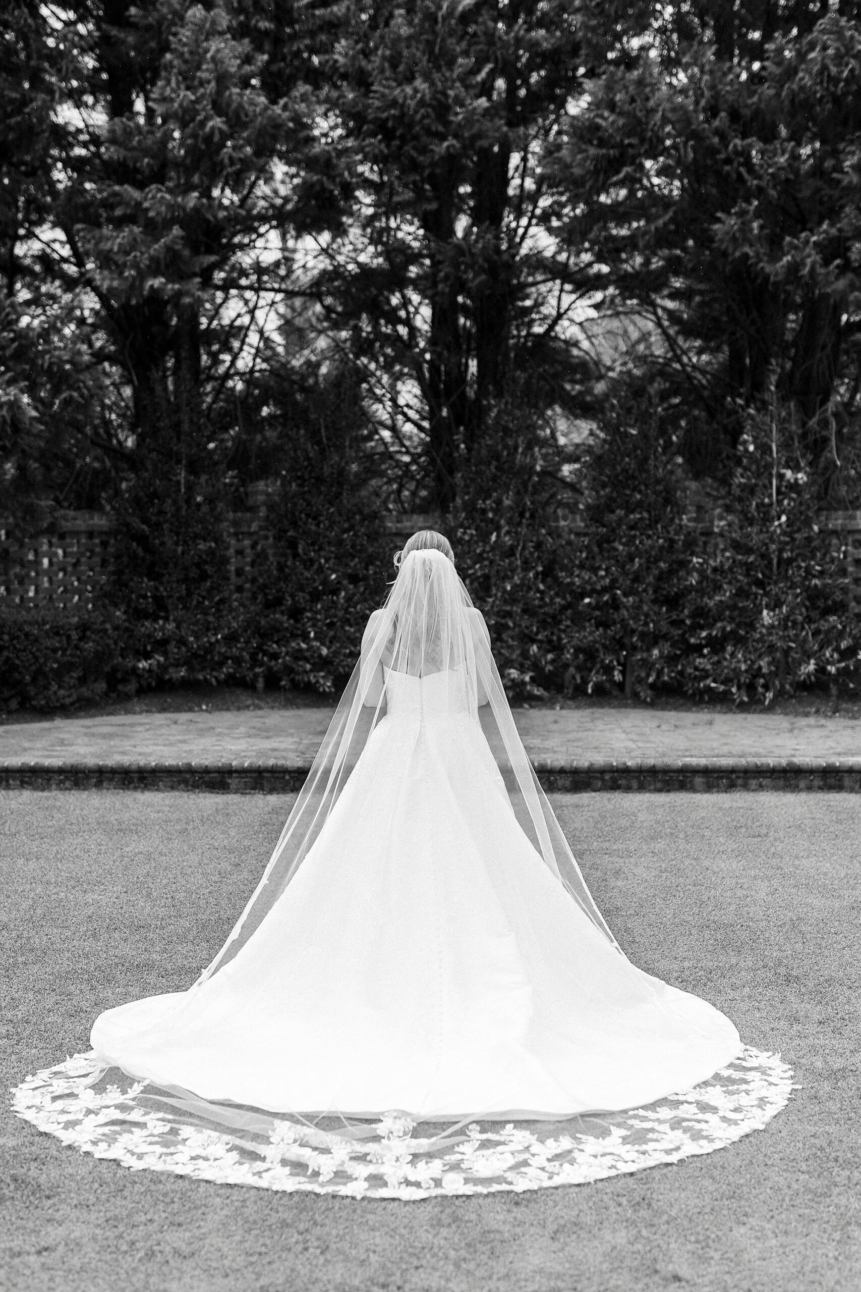 bride walks across lawn showing off veil and back of wedding gown