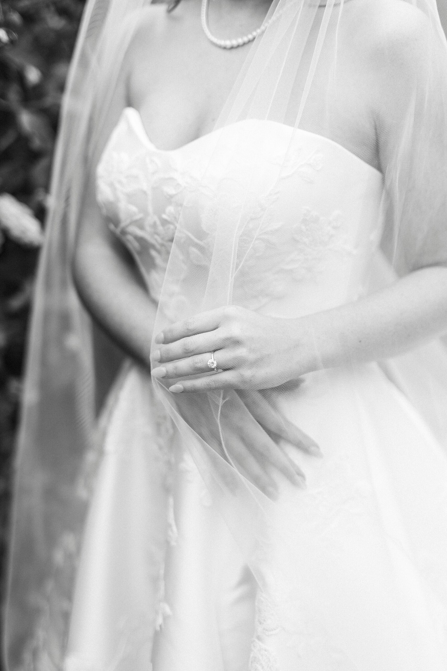bride pulls veils around shoulders and shows off engagement ring