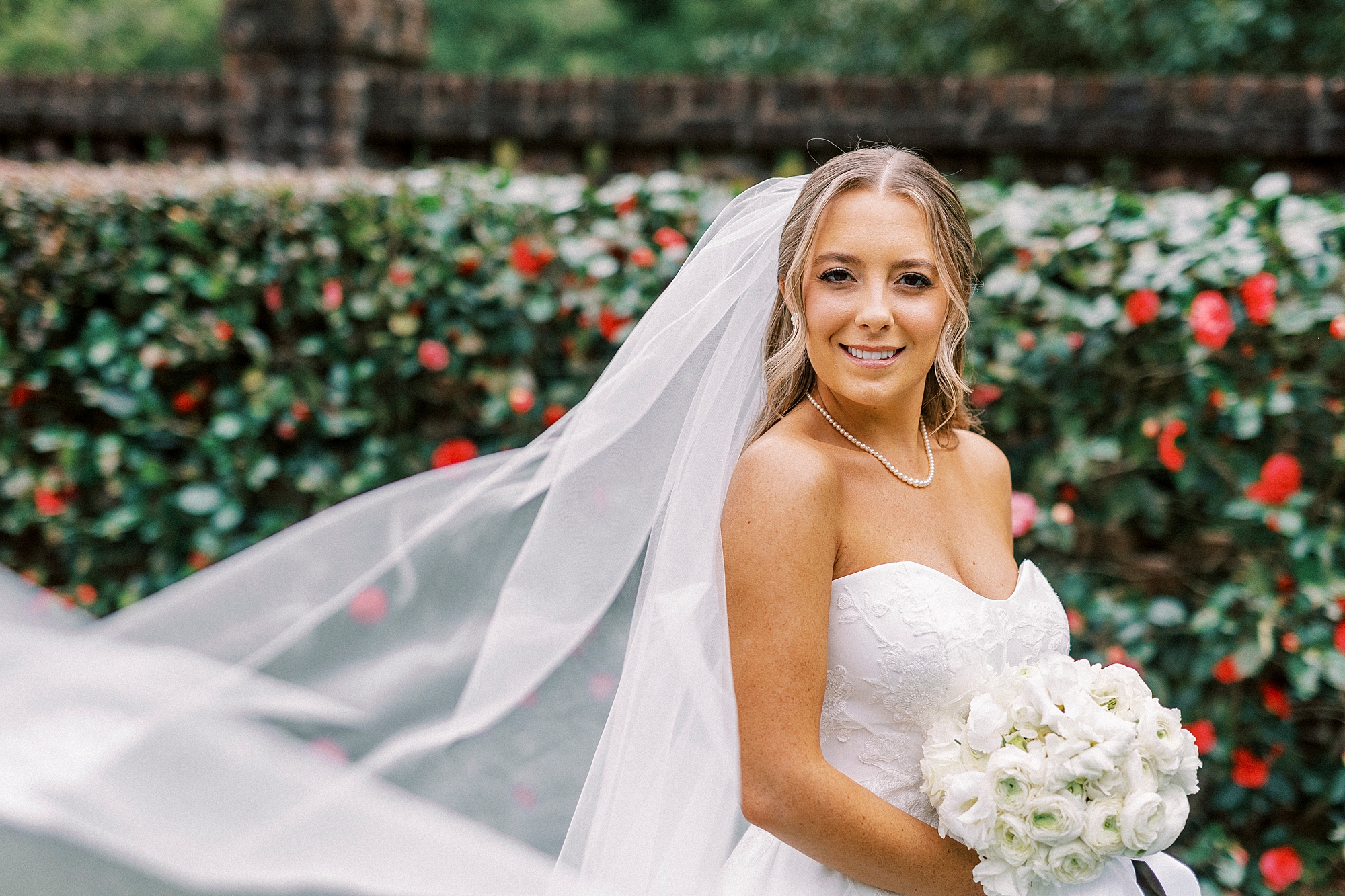 bride grins holding white bouquet with veil pulled behind her