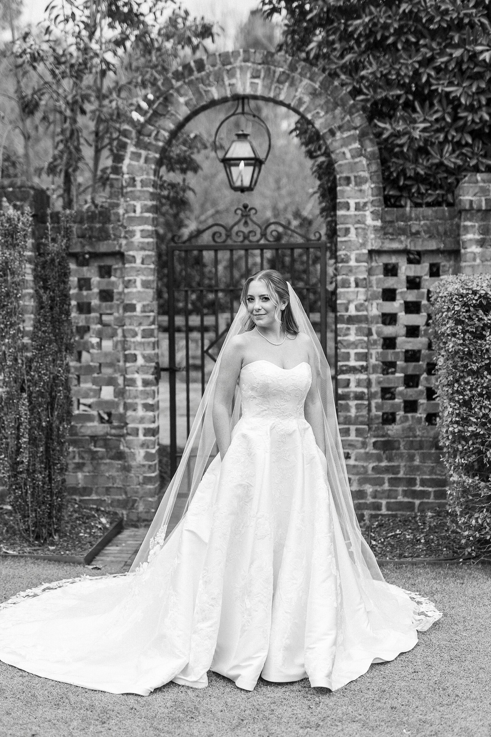bride stands in front of brick archway pulling veil around her shoulders 