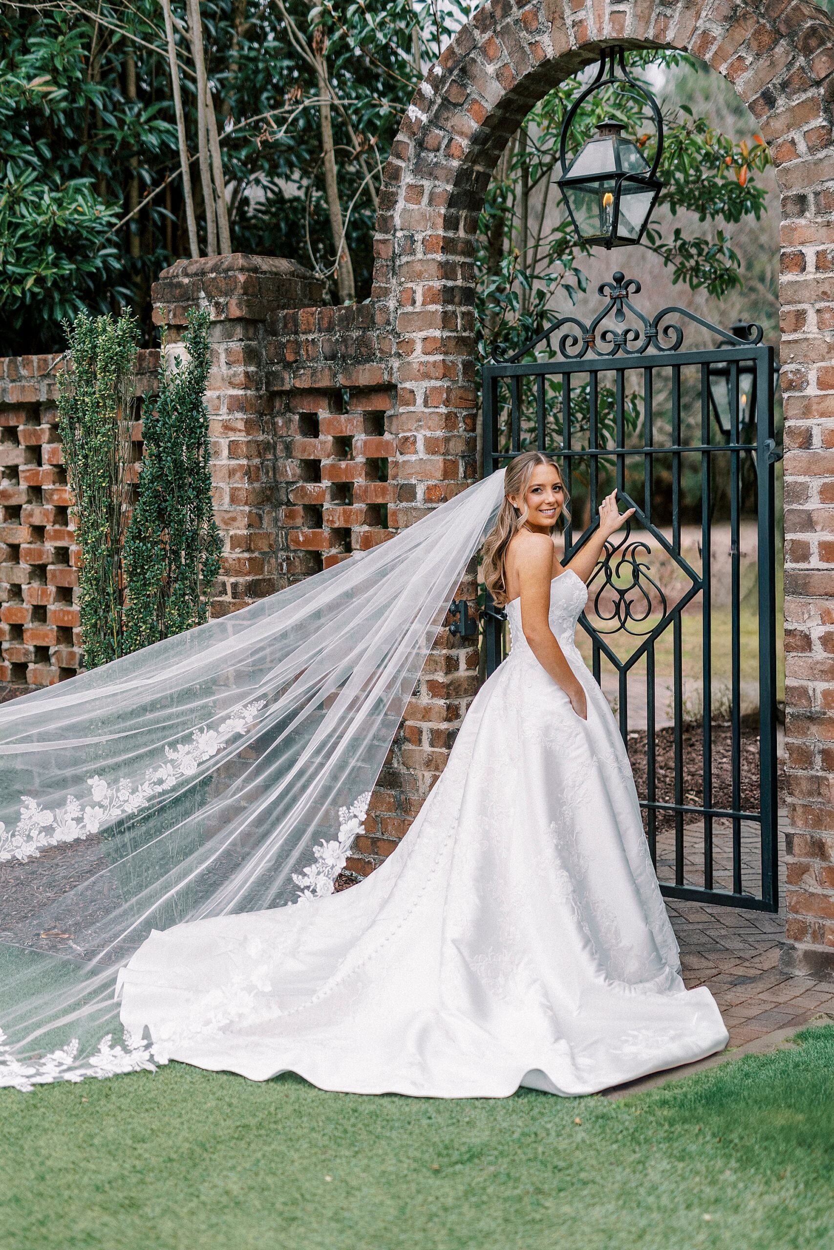 bride holds wrought iron gate in gardens of Wake Forest historic home
