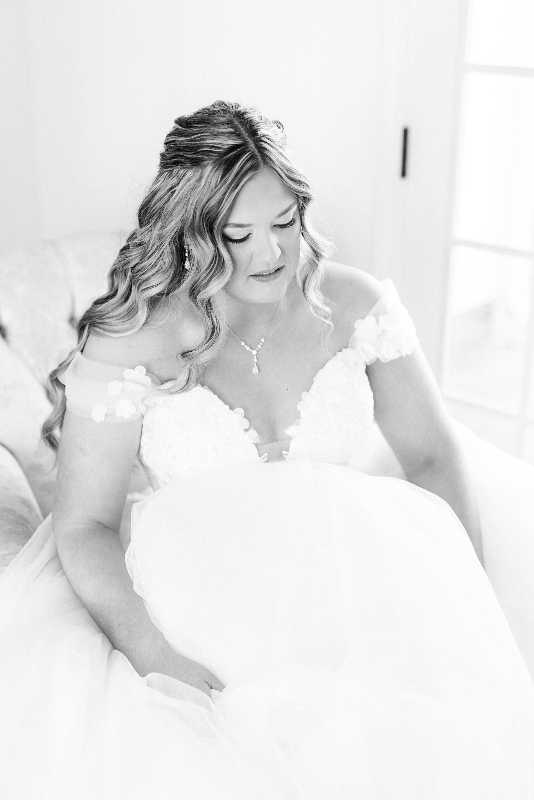 bride sits and adjusts skirt of wedding gown inside bridal suite 