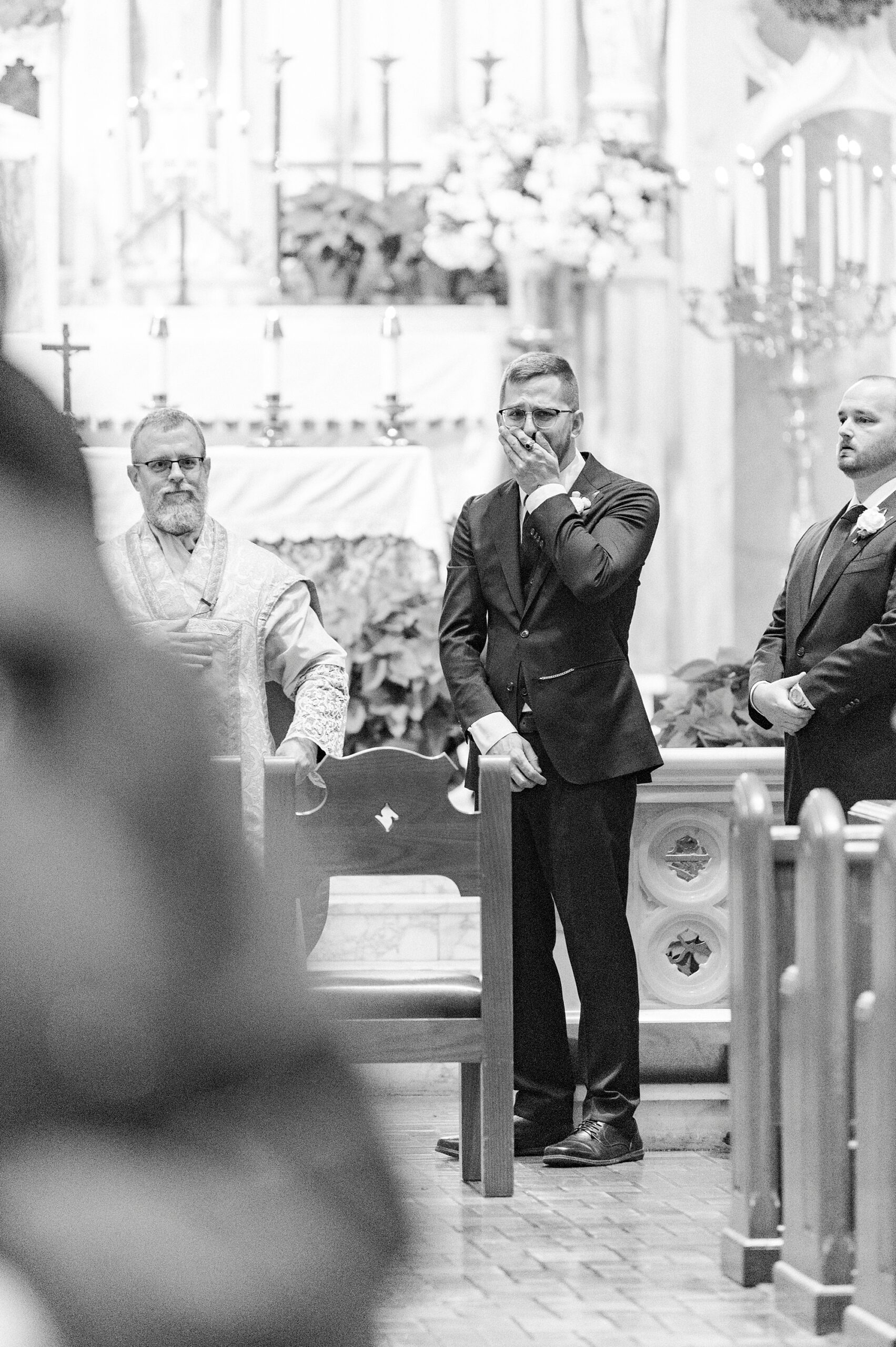 groom covers mouth reacting to seeing bride walk down aisle inside Our Lady of Grace