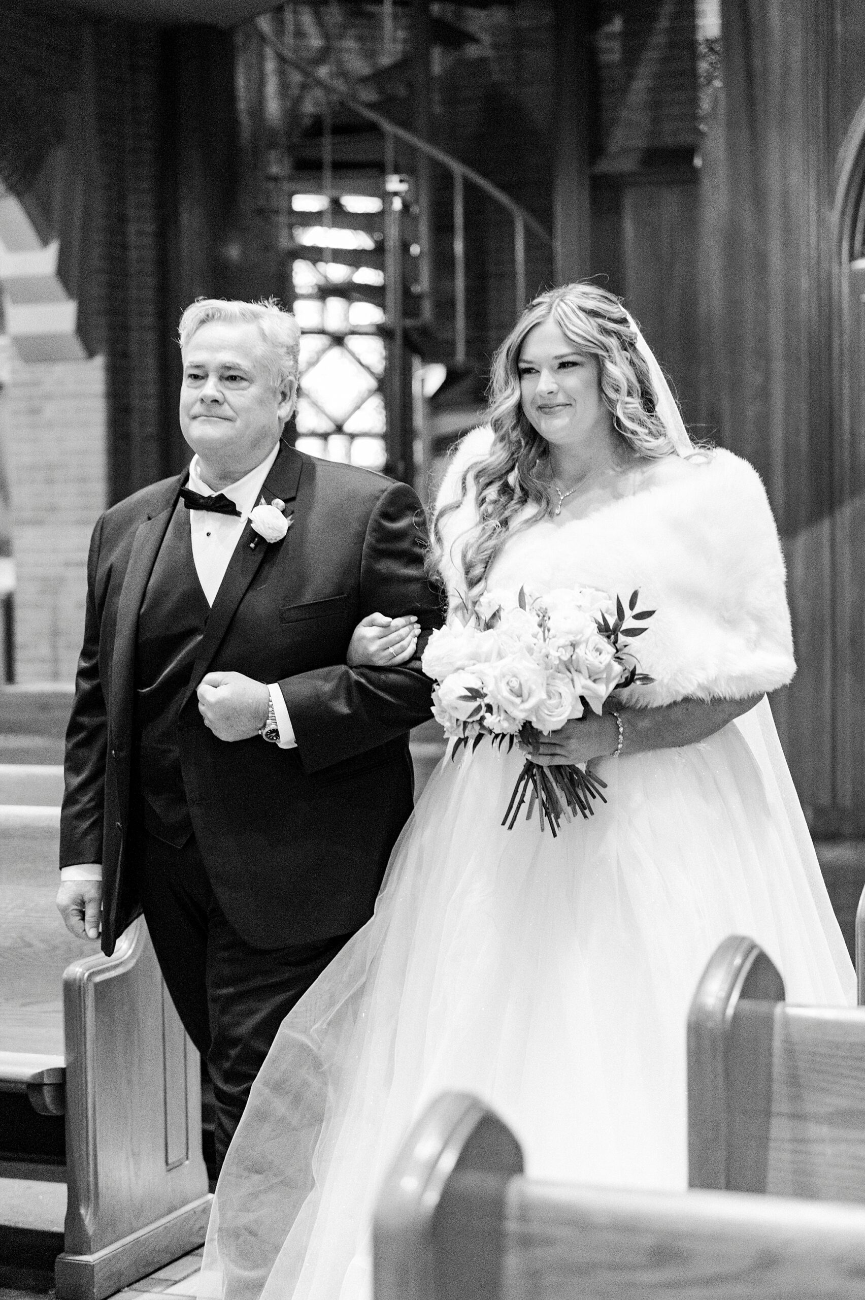 bride walks down aisle with father inside Our Lady of Grace wearing fur over wedding gown