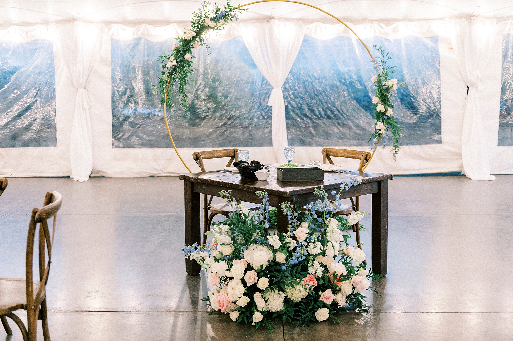 sweetheart table sits in front of gold arbor in tent at Summerfield Farms