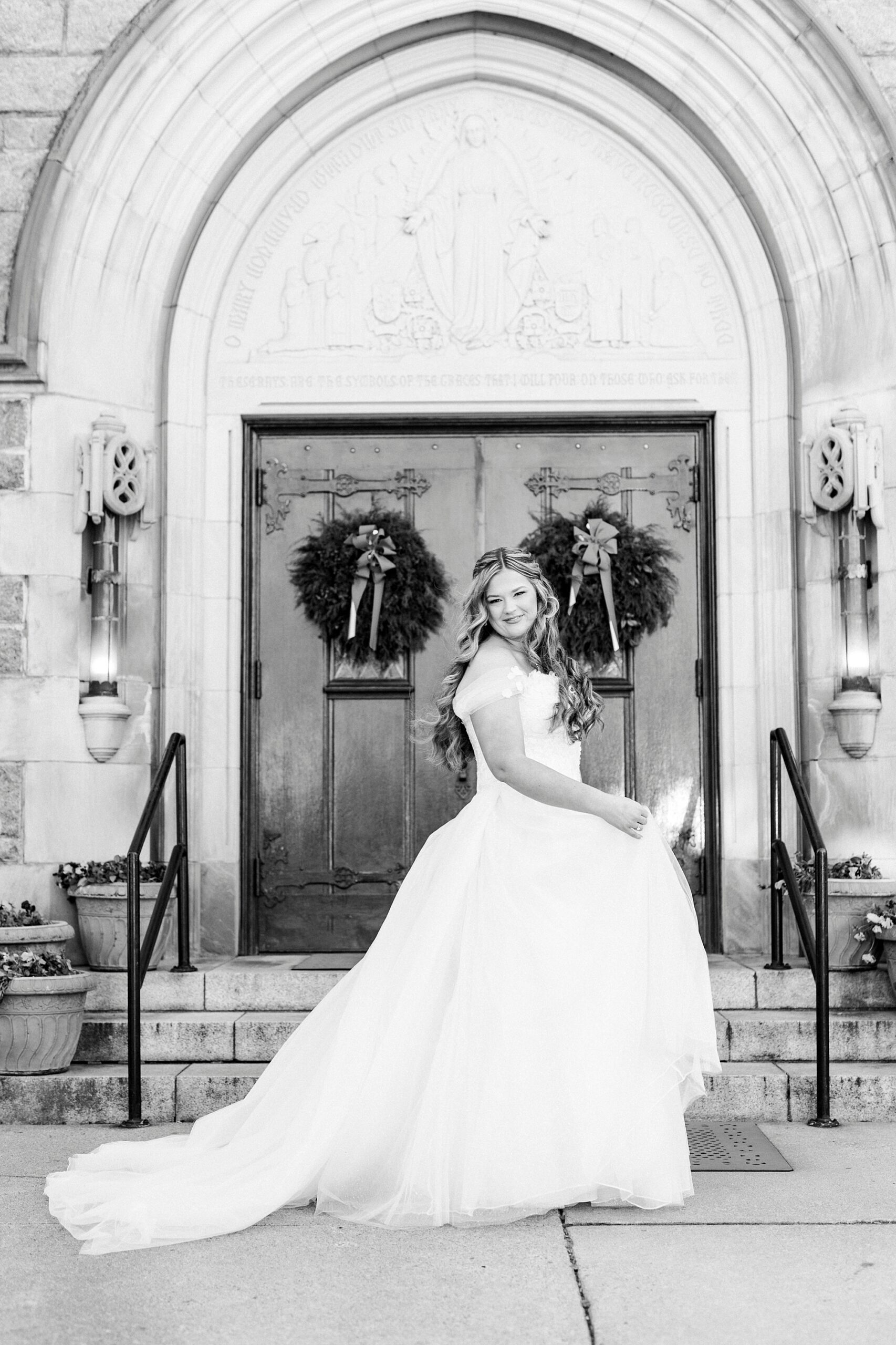 bride twirls wedding gown outside Our Lady of Grace with wreaths on the doors