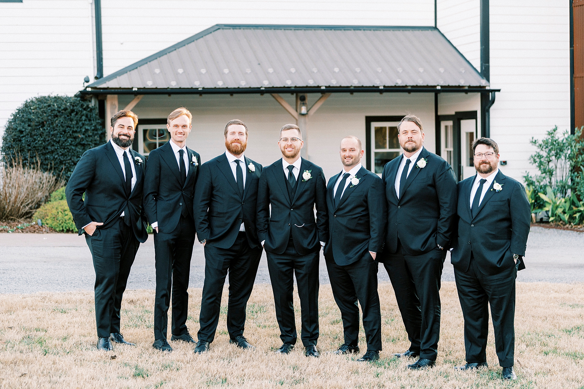groom and groomsmen stand in suits outside Summerfield Farms