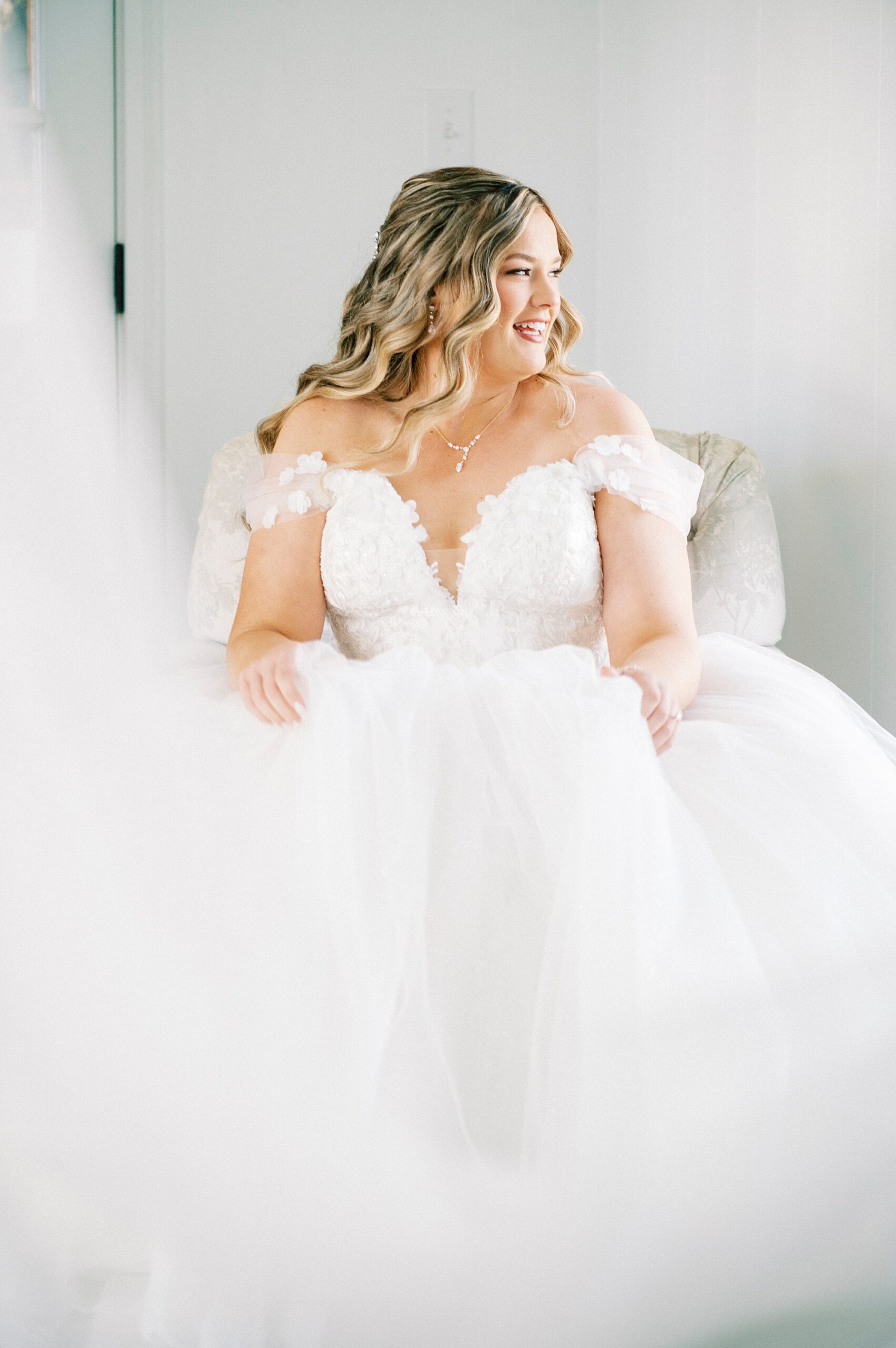 bride sits with wedding gown holding veil out in front of her