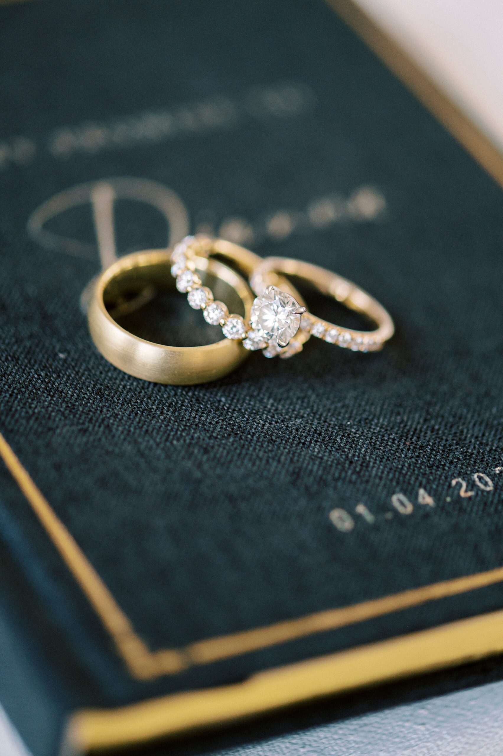 gold wedding bands rest on green and gold vow booklet 