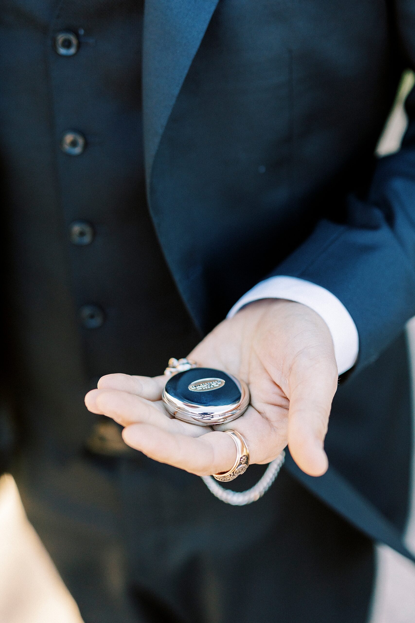 man holds out silver pocket watch during winter wedding day