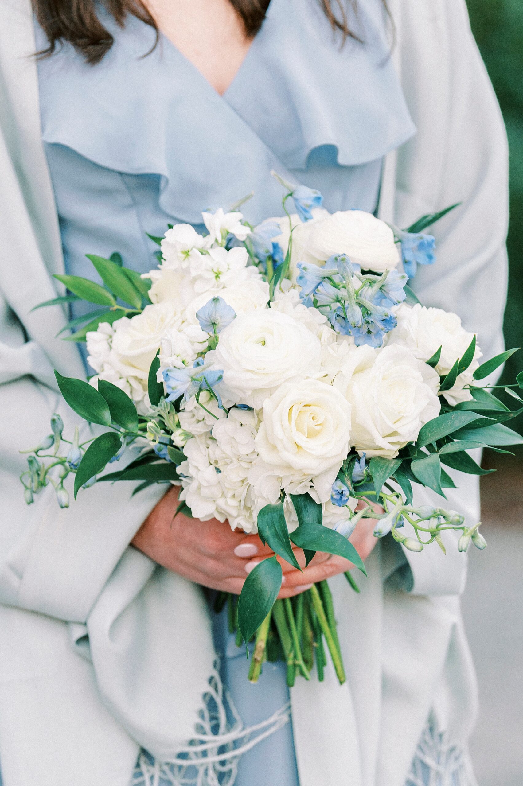 bridesmaid in blue dress with wrap holds bouquet of white and blue flowers for winter wedding