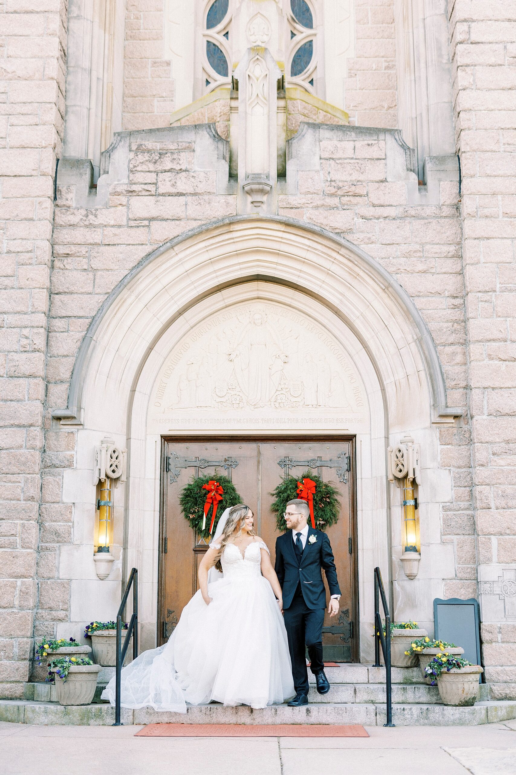 bride and groom hold hands walking down staircase outside Our Lady of Grace