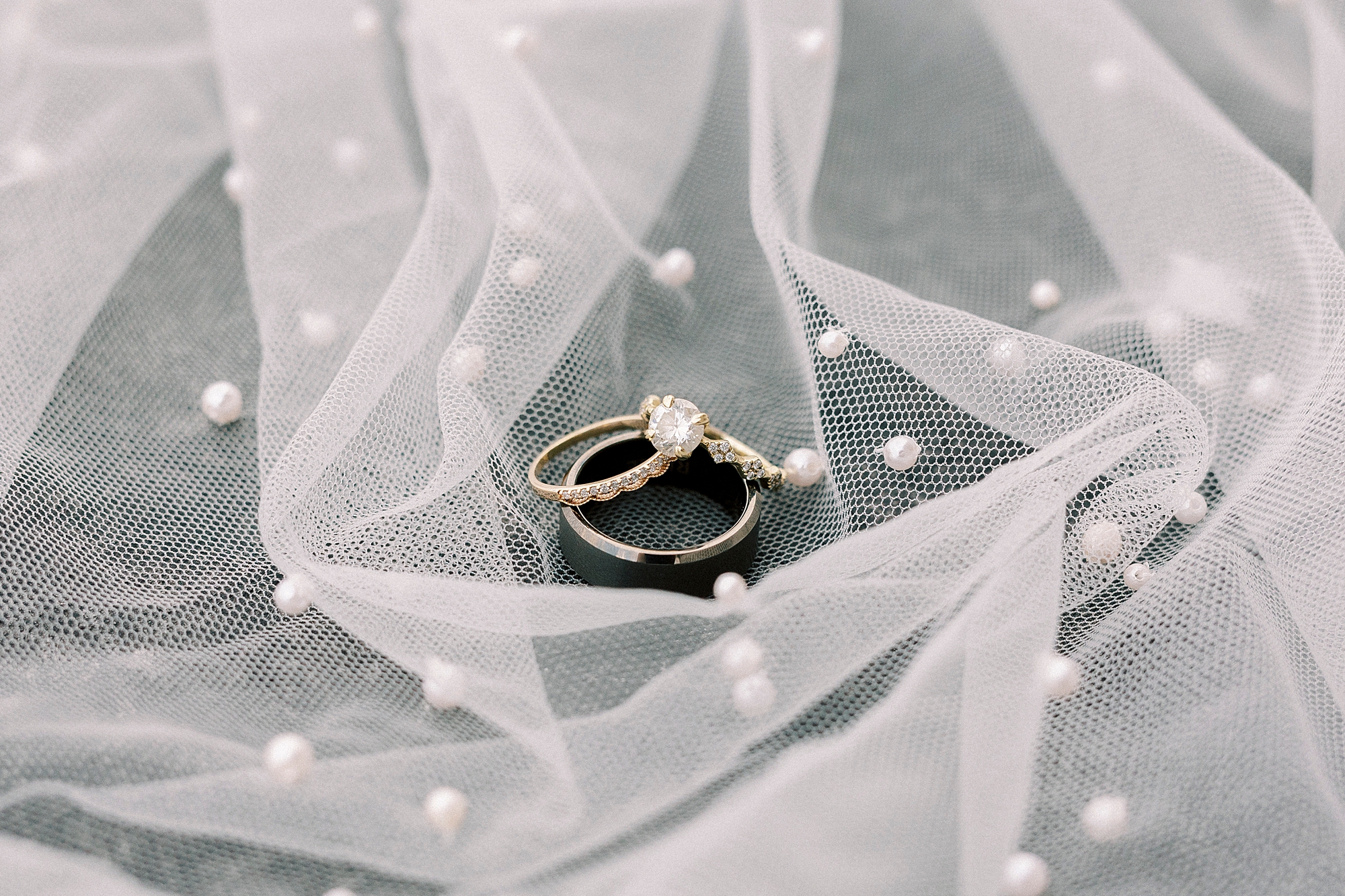 wedding bands sit on bride's veil with pearl accents 