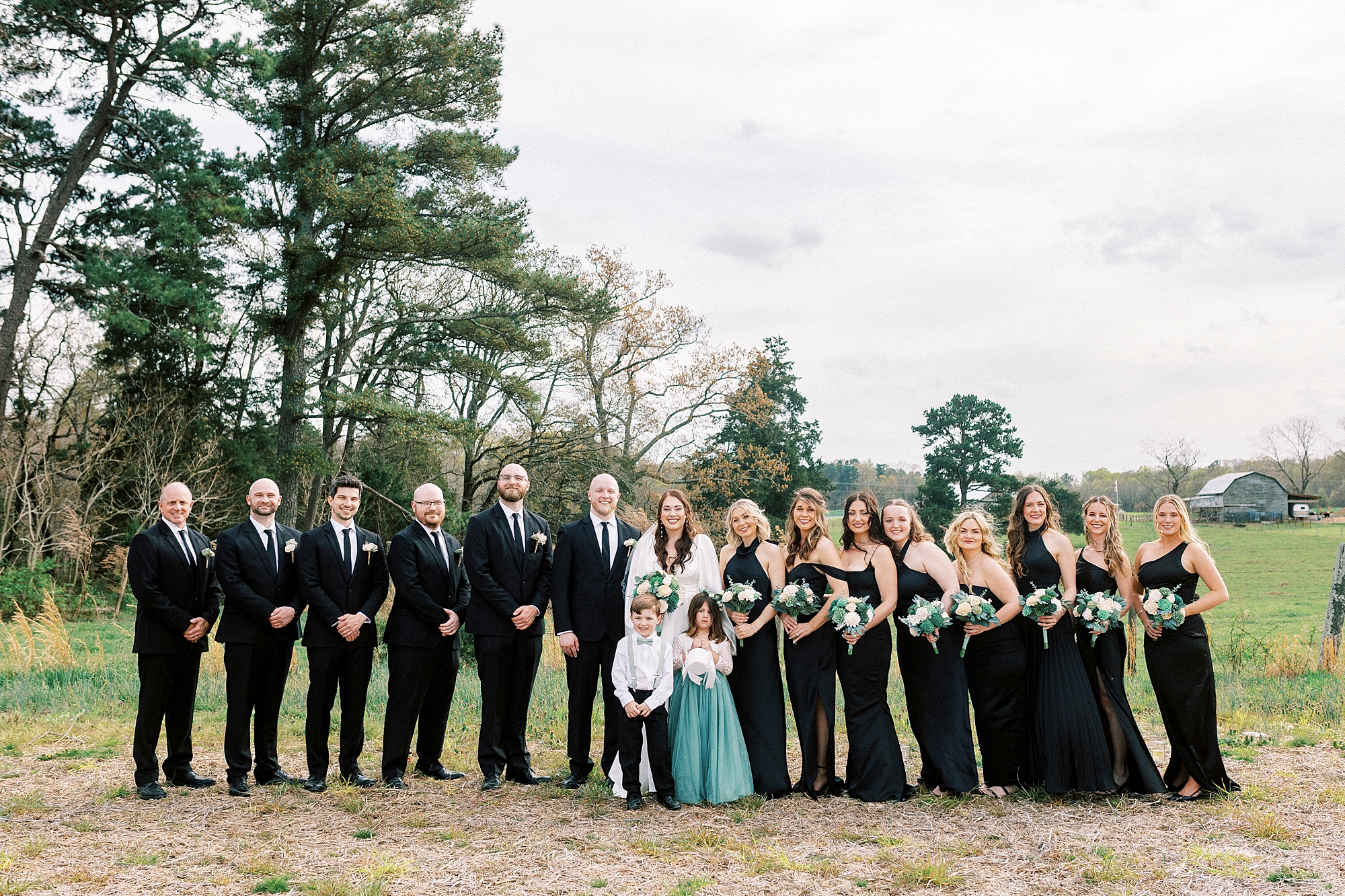 bride and groom stand with wedding party in black attire with green accents 