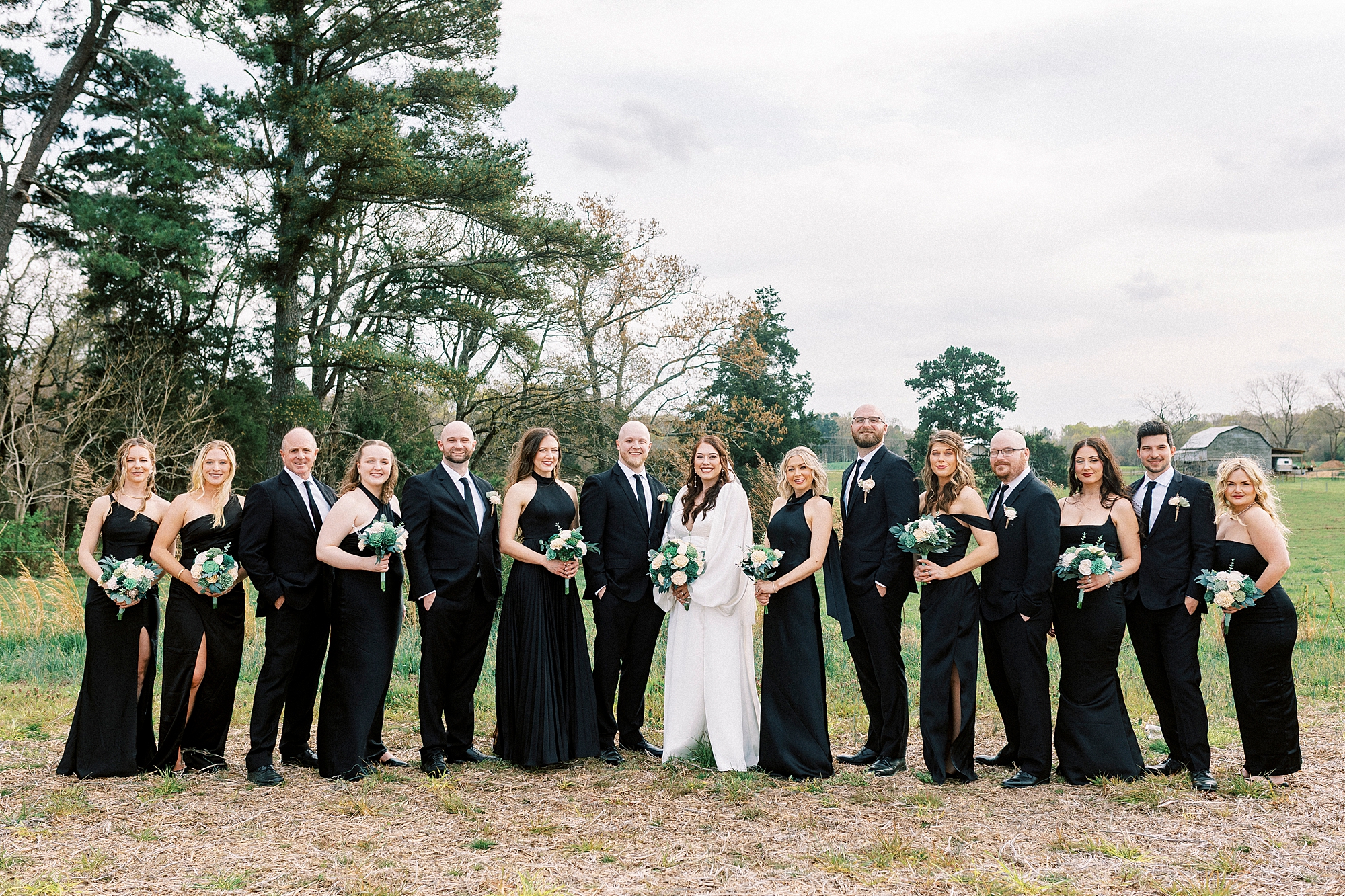 bride poses with bridesmaids in black dresses in pasture at Sixty Acres Farm