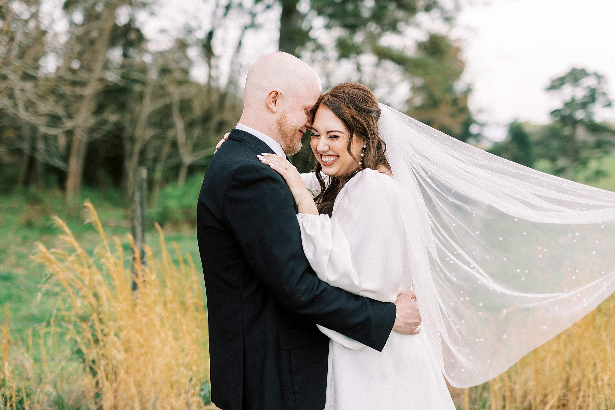 groom hugs bride to him while she laughs and veil floats behind her