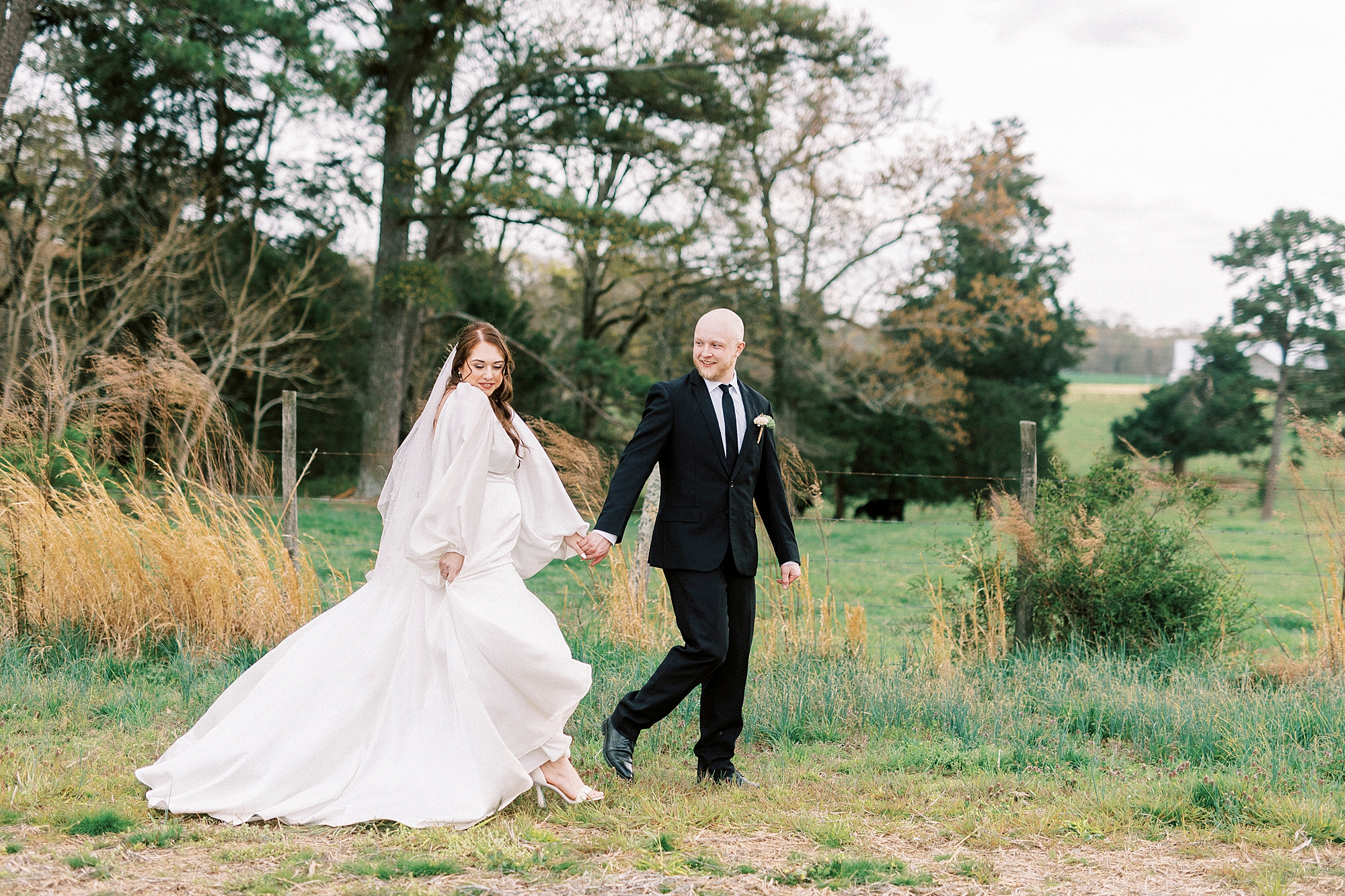 bride and groom hold hands walking along edge of pasture at Sixty Acres Farm