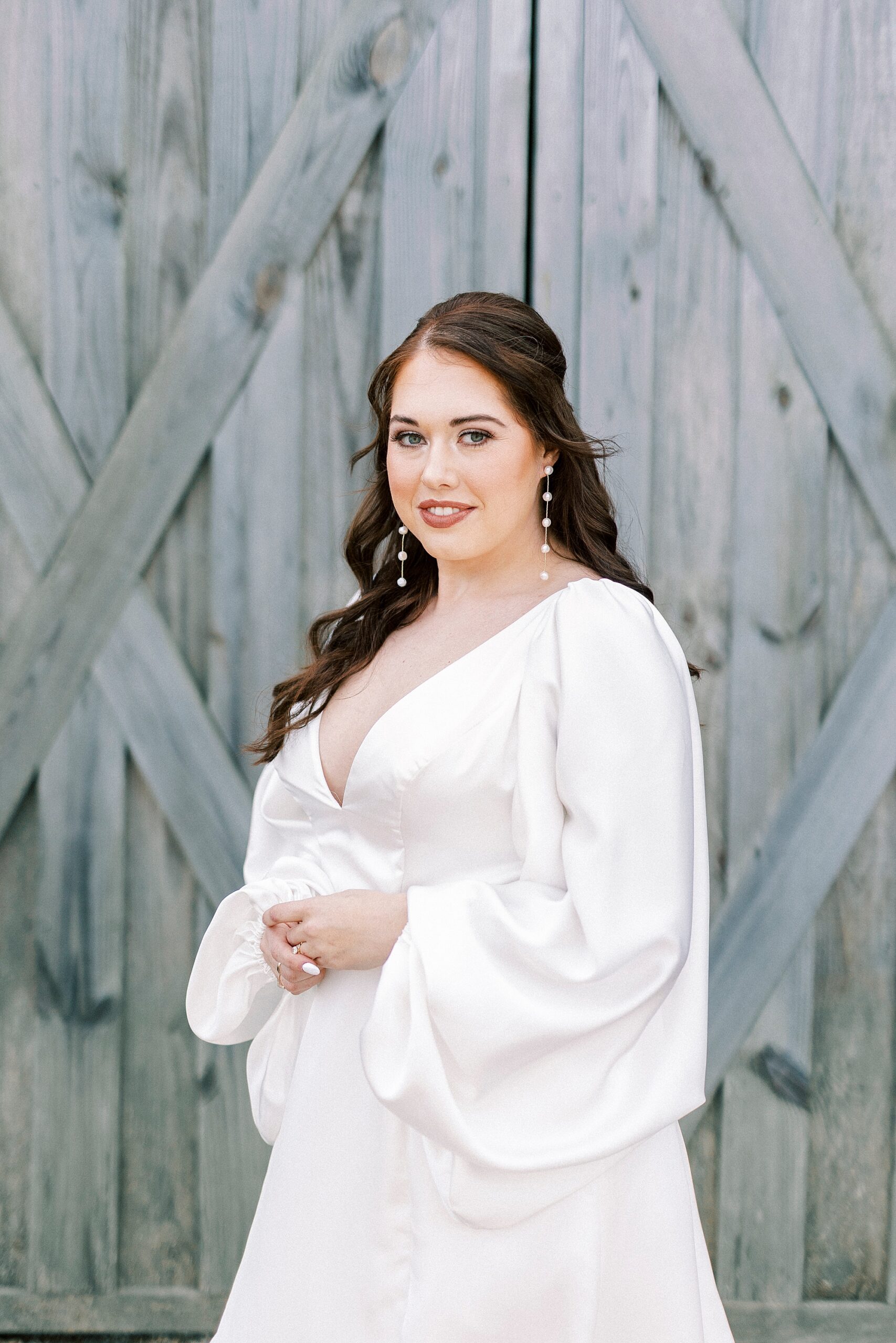 bride smiles in long sleeve wedding gown in front of barn doors 