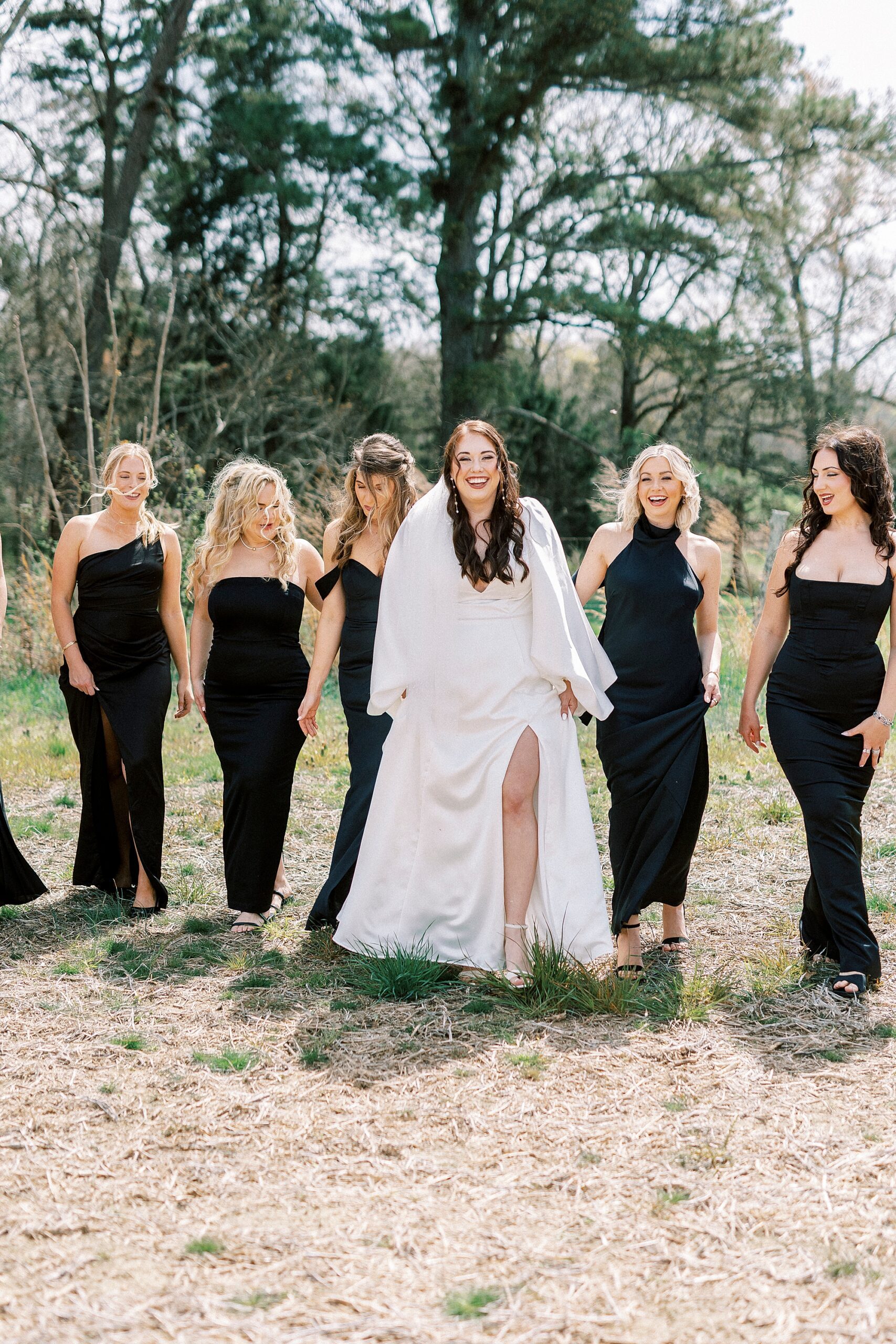 bride walks with bridesmaids in black gowns at Sixty Acres Farm