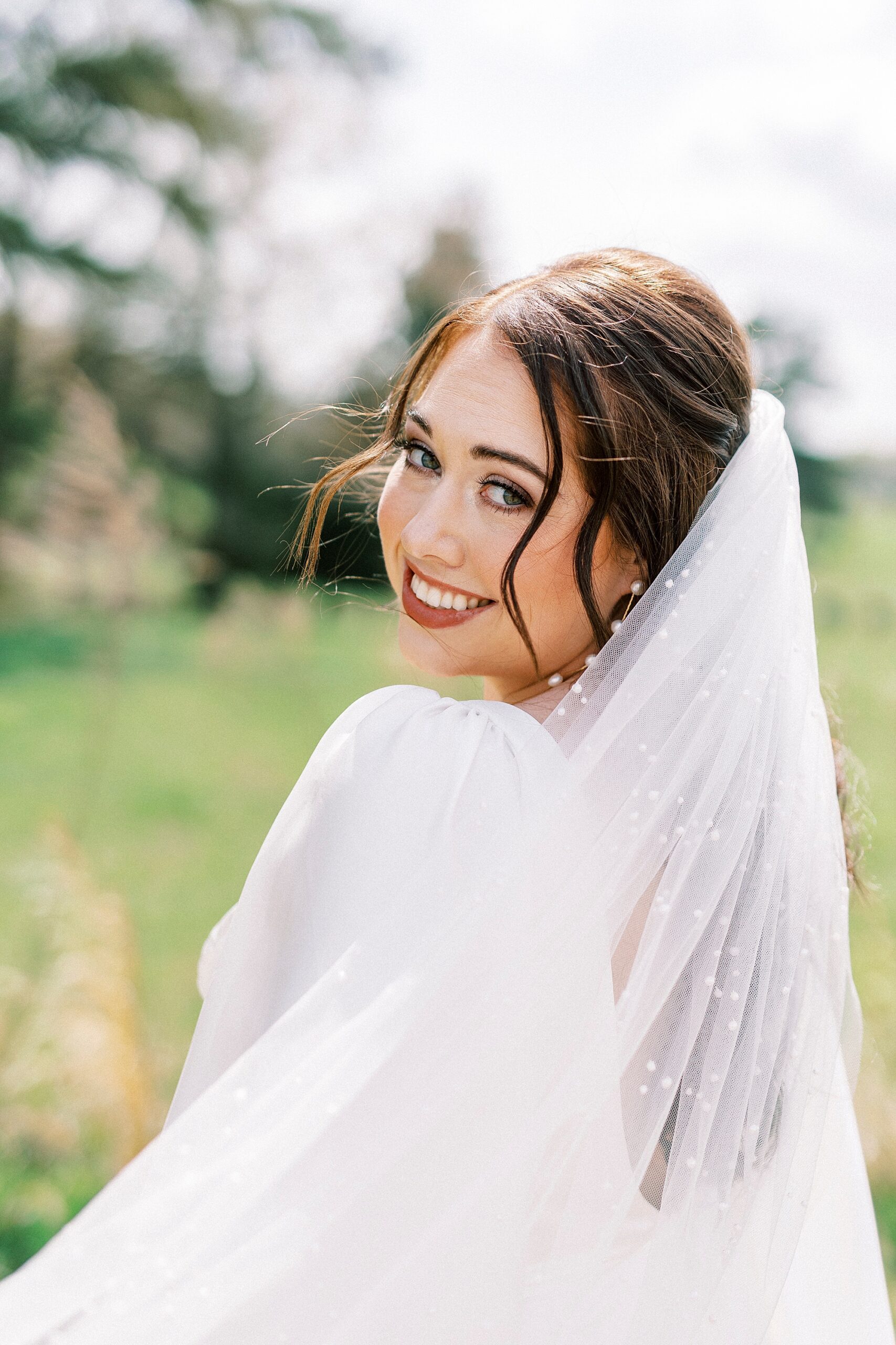 brunette bride looks over shoulder with veil pulled around her 