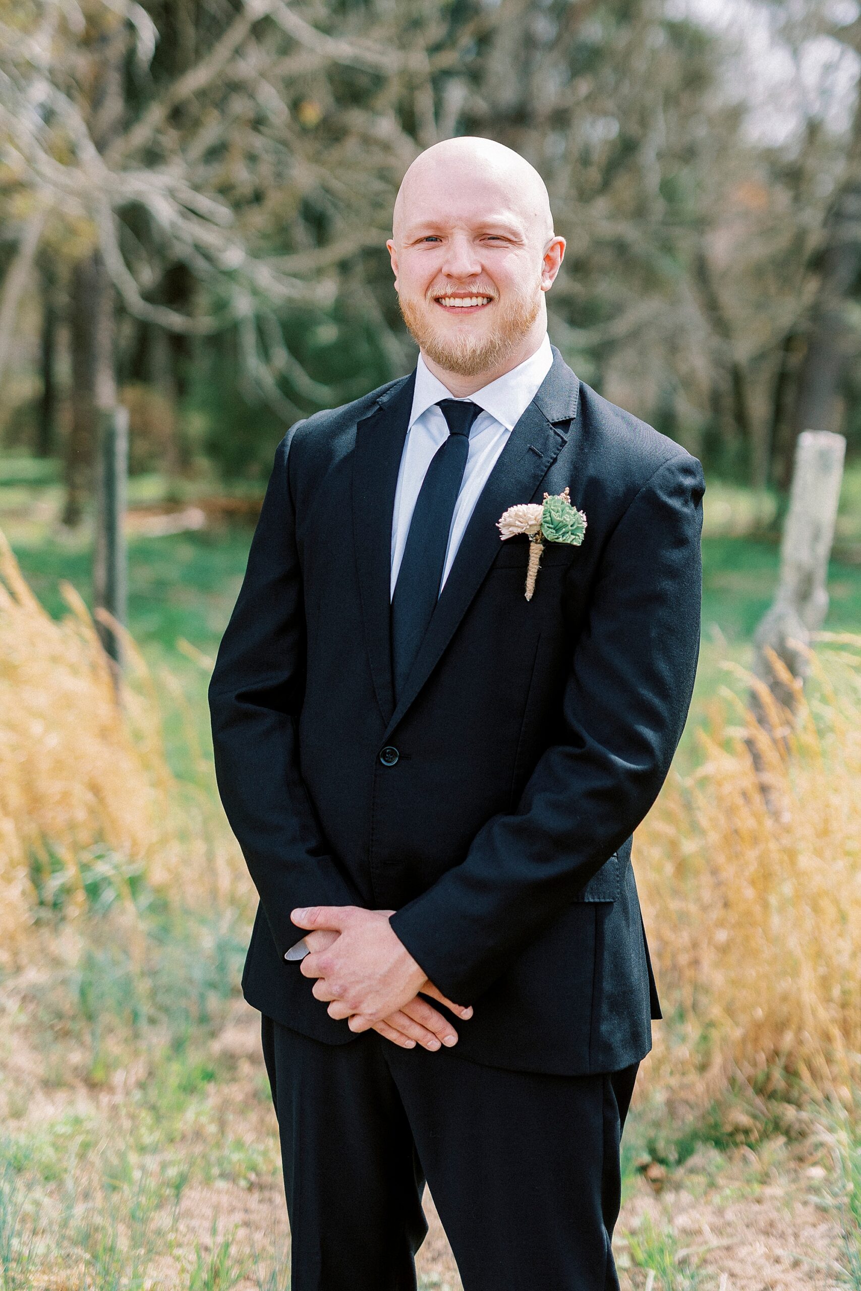 groom stands in black suit before wedding day at Sixty Acres Farm