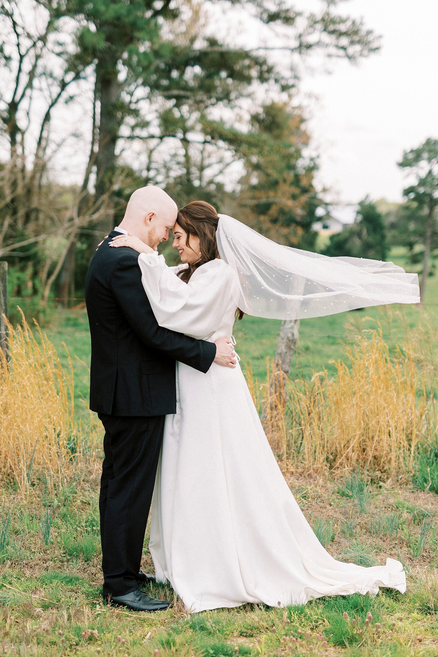 bride and groom lean heads together while bride's veil floats behind them