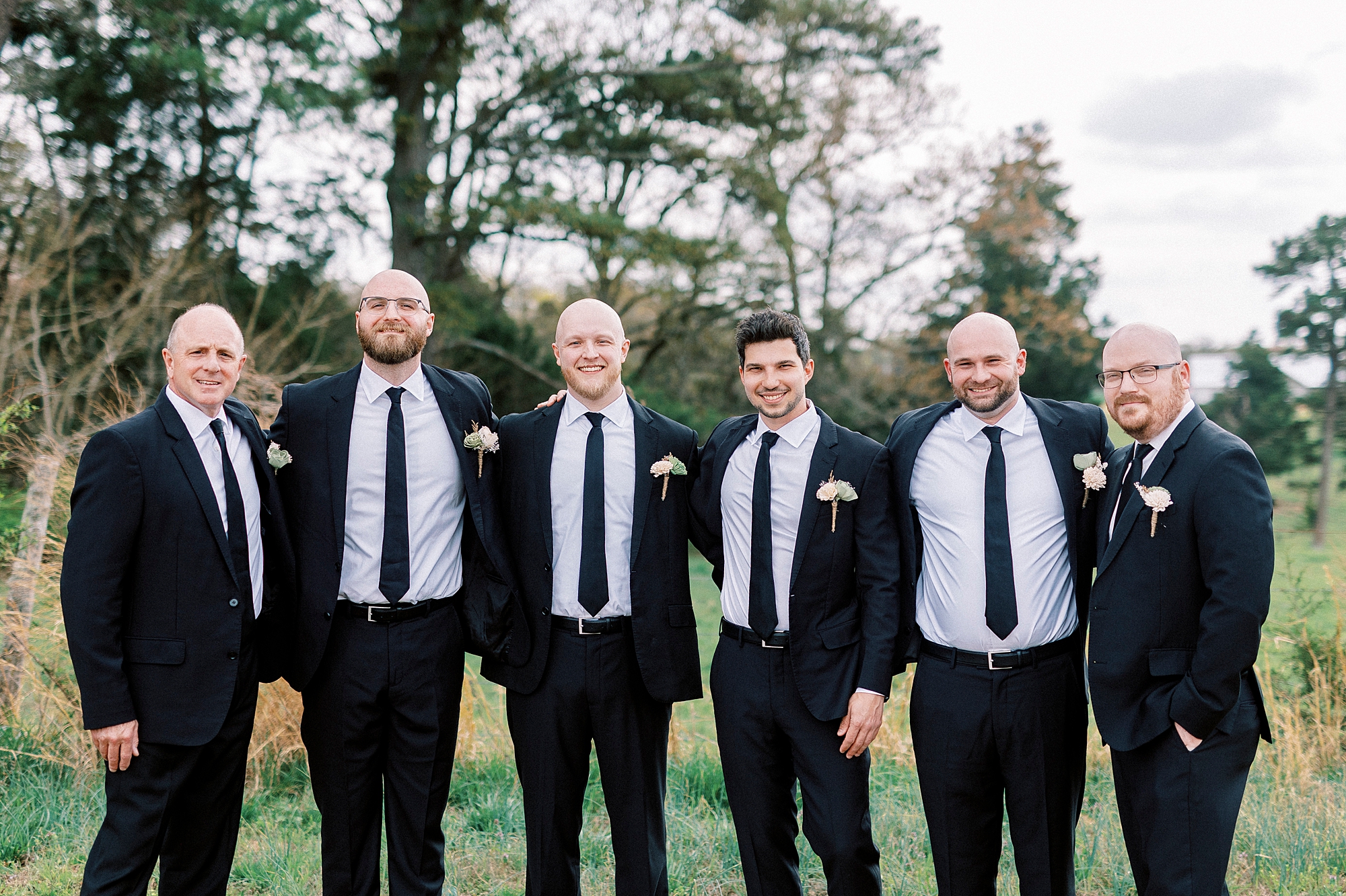 groom and groomsmen stand hugging each other in black suits 