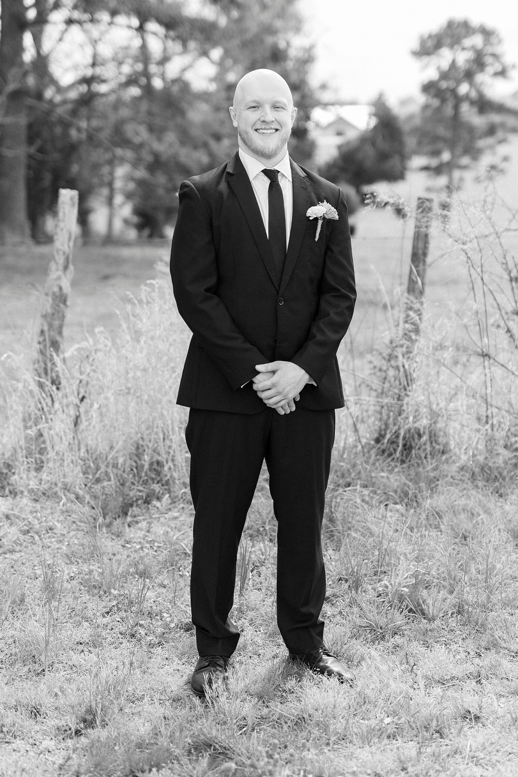 groom stands in pasture with hands in front of his suit at Sixty Acres Farm