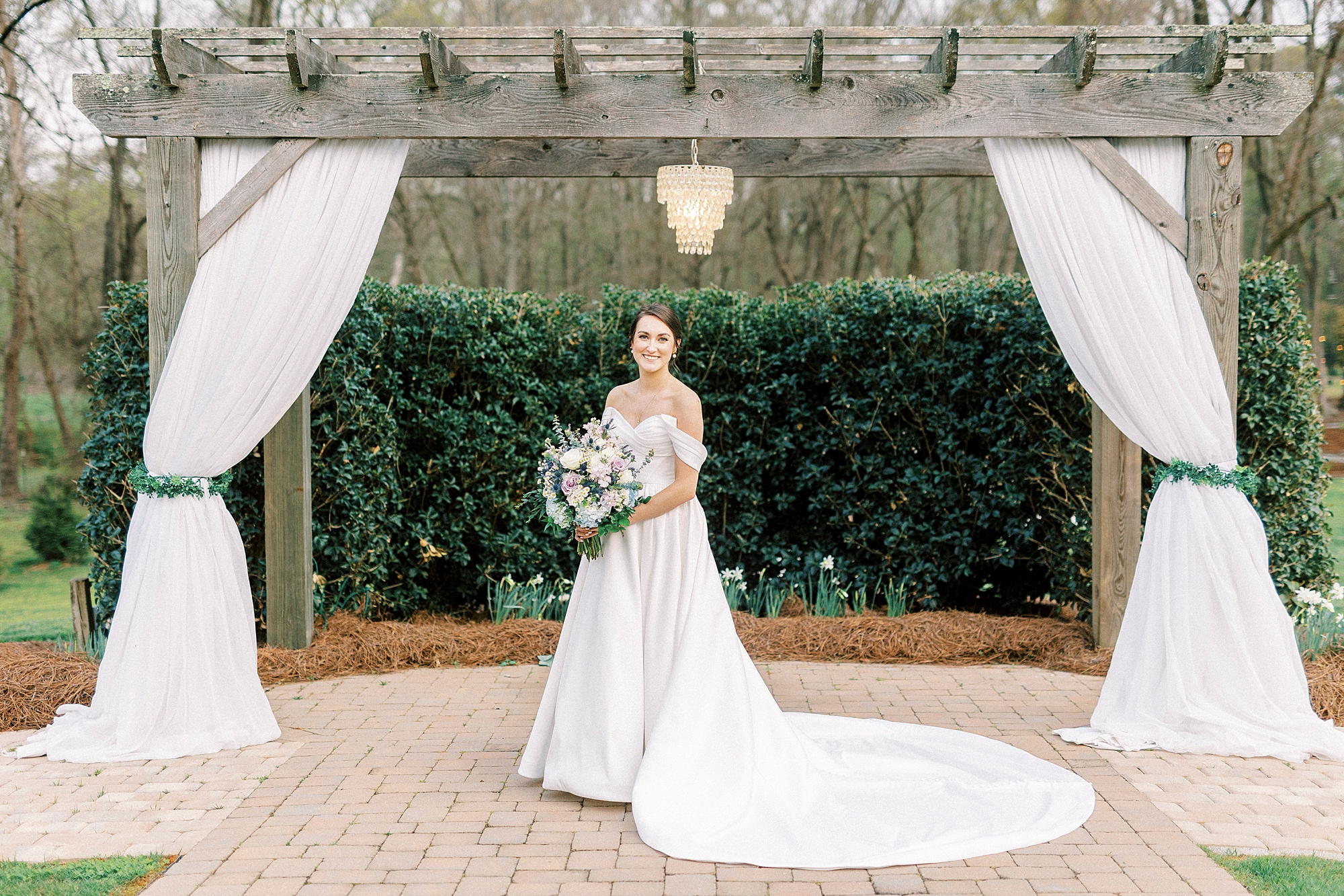 bride holds bouquet of white and purple flowers under wooden gazebo at Low Meadows Estate
