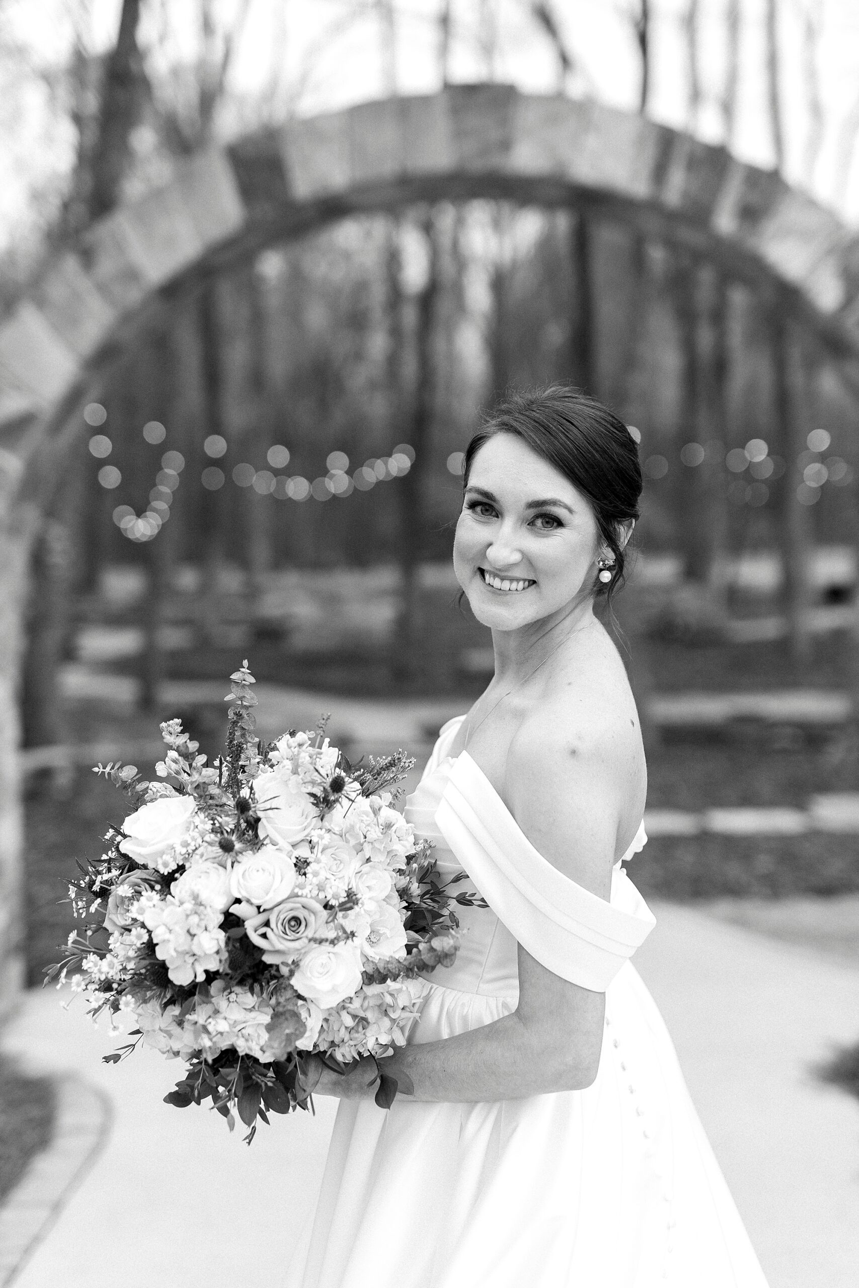 bride looks over shoulder in wedding gown holding bouquet in garden at Low Meadows Estate