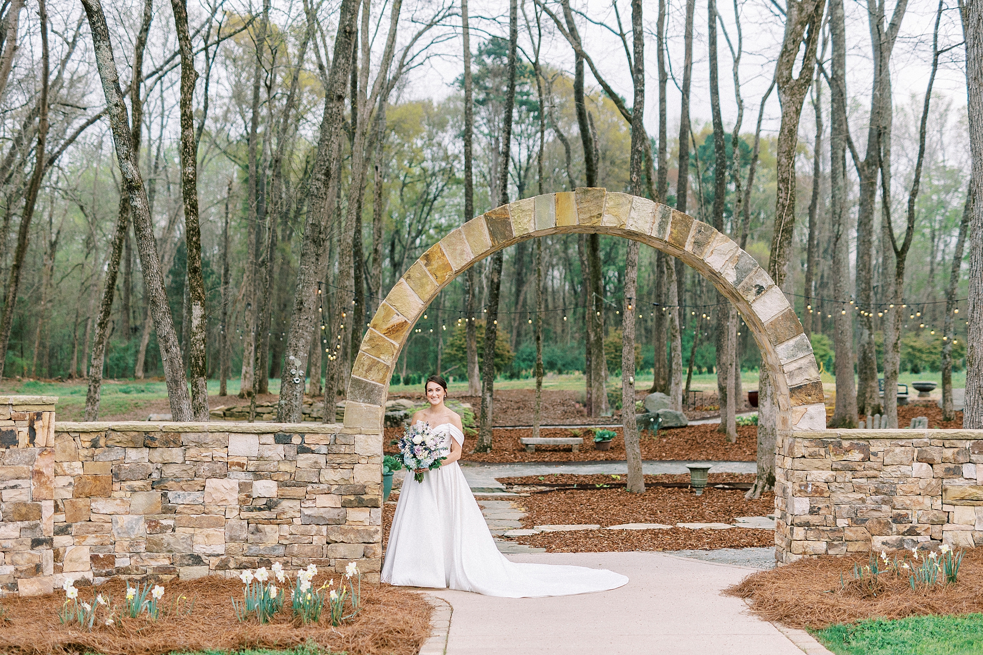 bride leans against stone archway in gardens of Low Meadows Estate