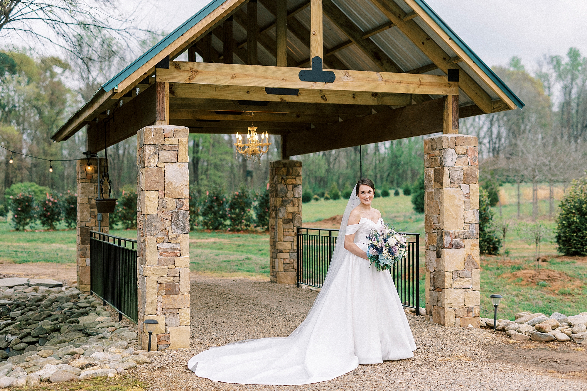 bride poses between stone arches of bridge at Low Meadows Estate