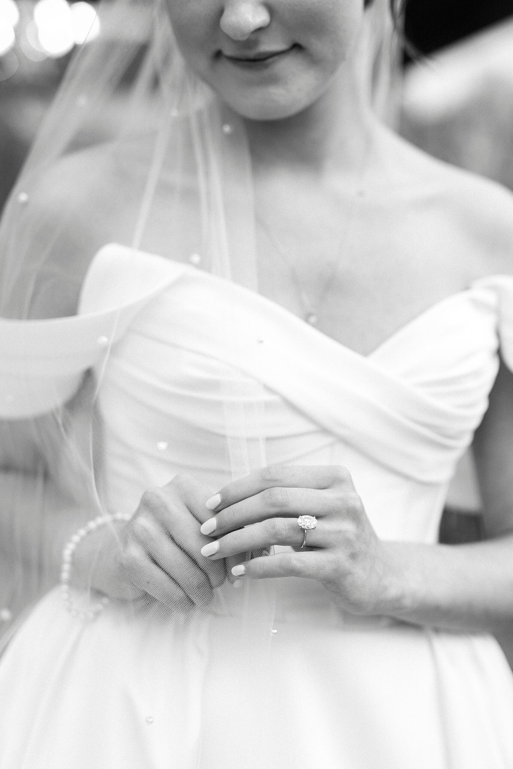 black and white photo of bride holding veil showing off ring