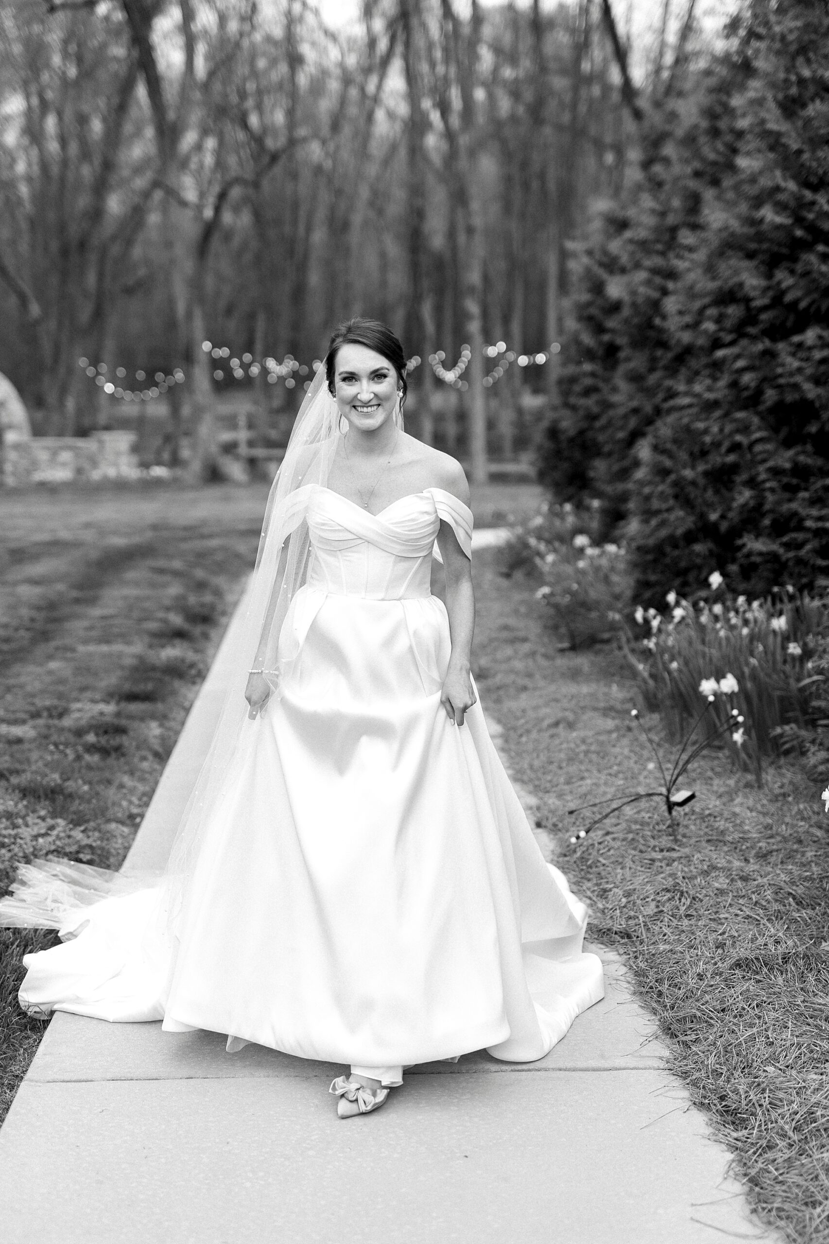 bride walks down sidewalk holding up skirt of wedding dress