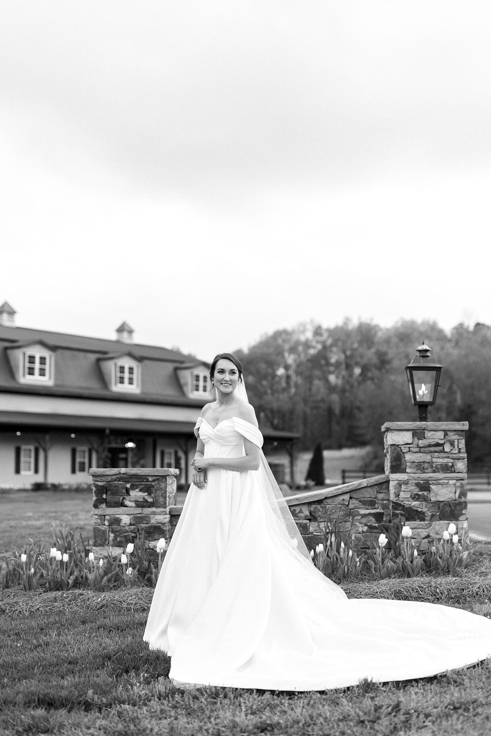 bride stands by welcome gate and farmhouse at Low Meadows Estate