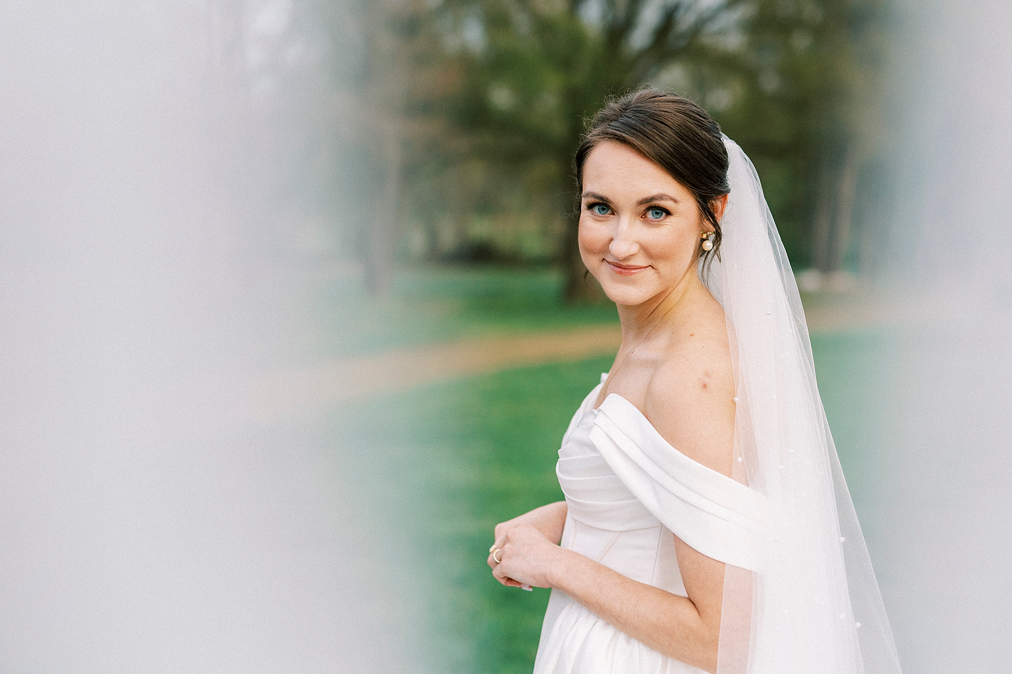 bride smiles over shoulder with veil pulled in front of camera 
