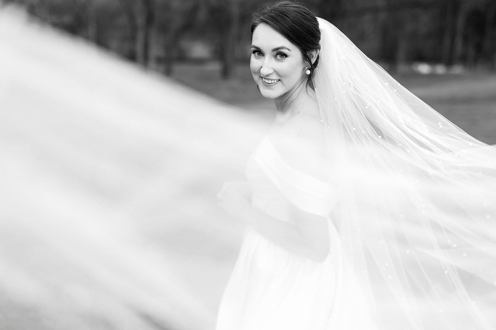 bride smiles over shoulder with veil pulled around her