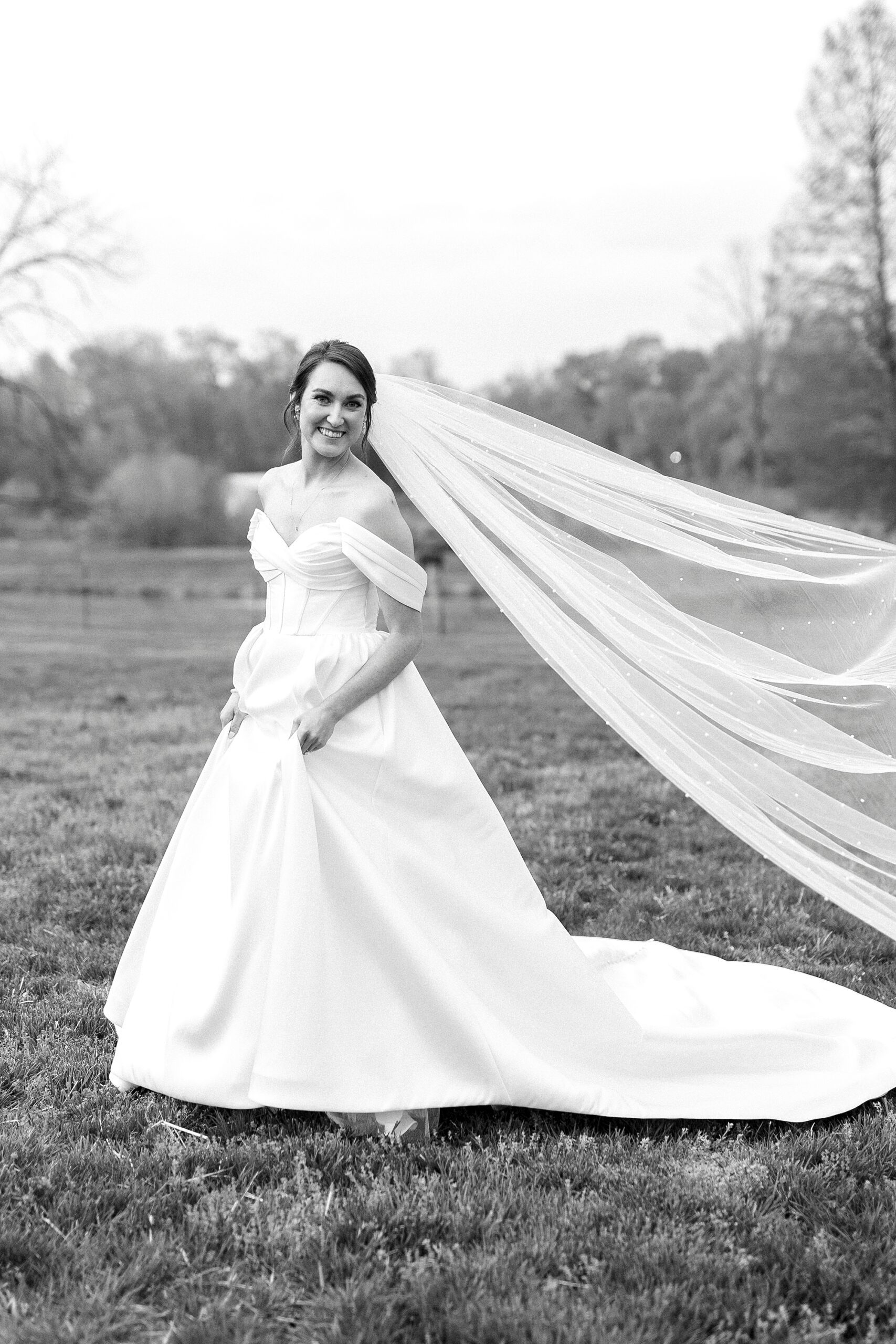 bride smiles pulling skirt around her on lawn at Low Meadows Estate