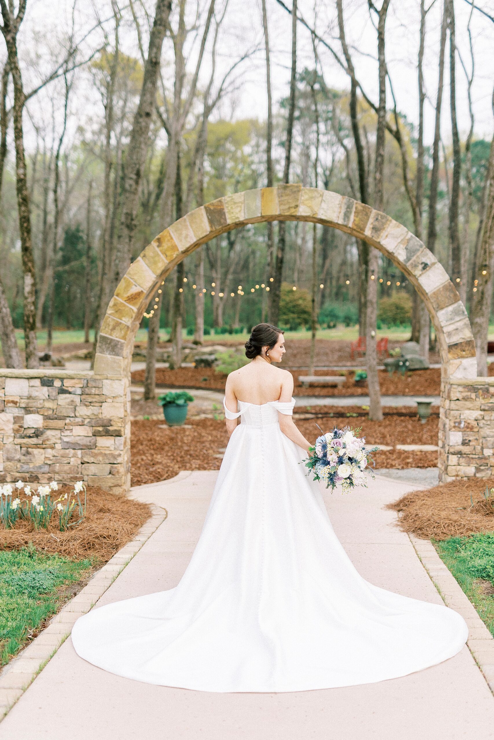 bride faces arch and looks over her shoulder with bouquet by her hip