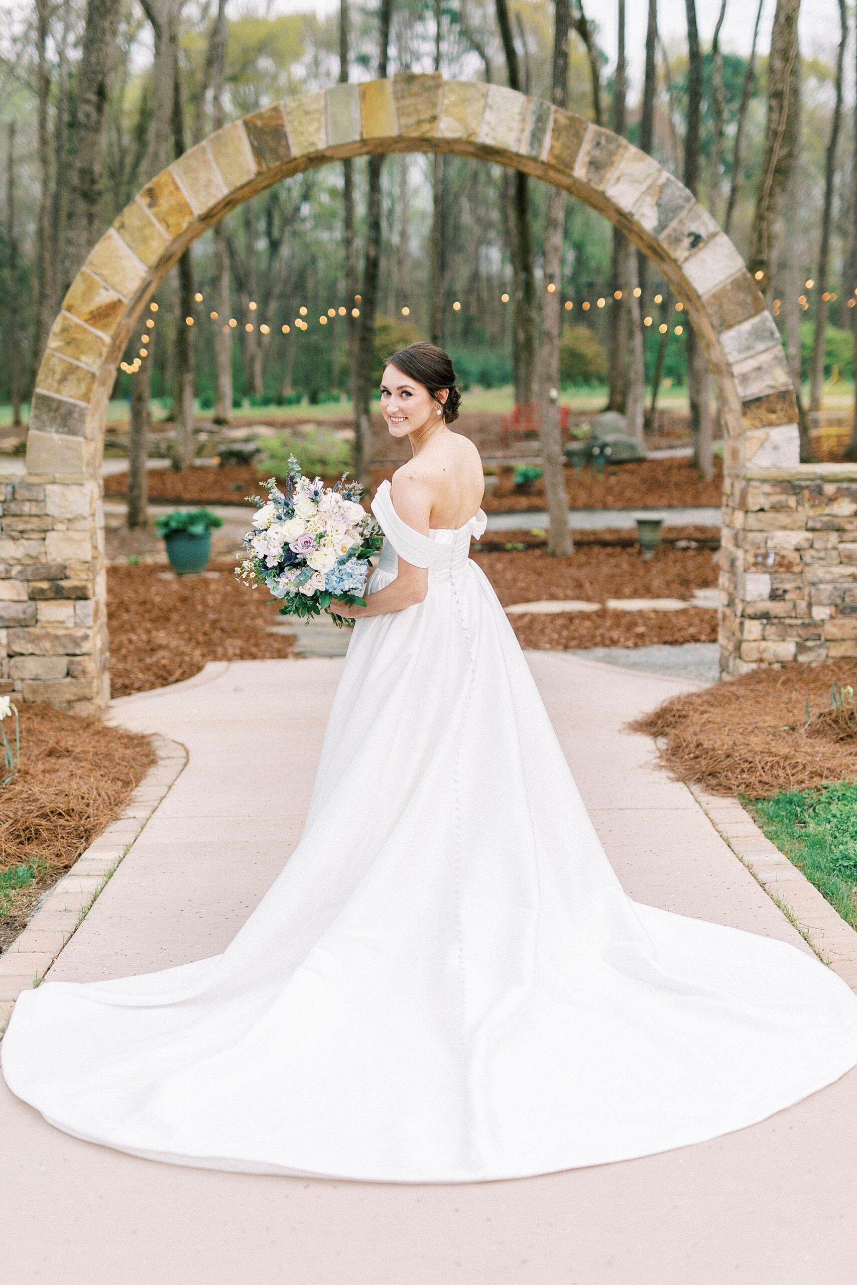 bride poses by stone arbor in gardens of Low Meadows Estate