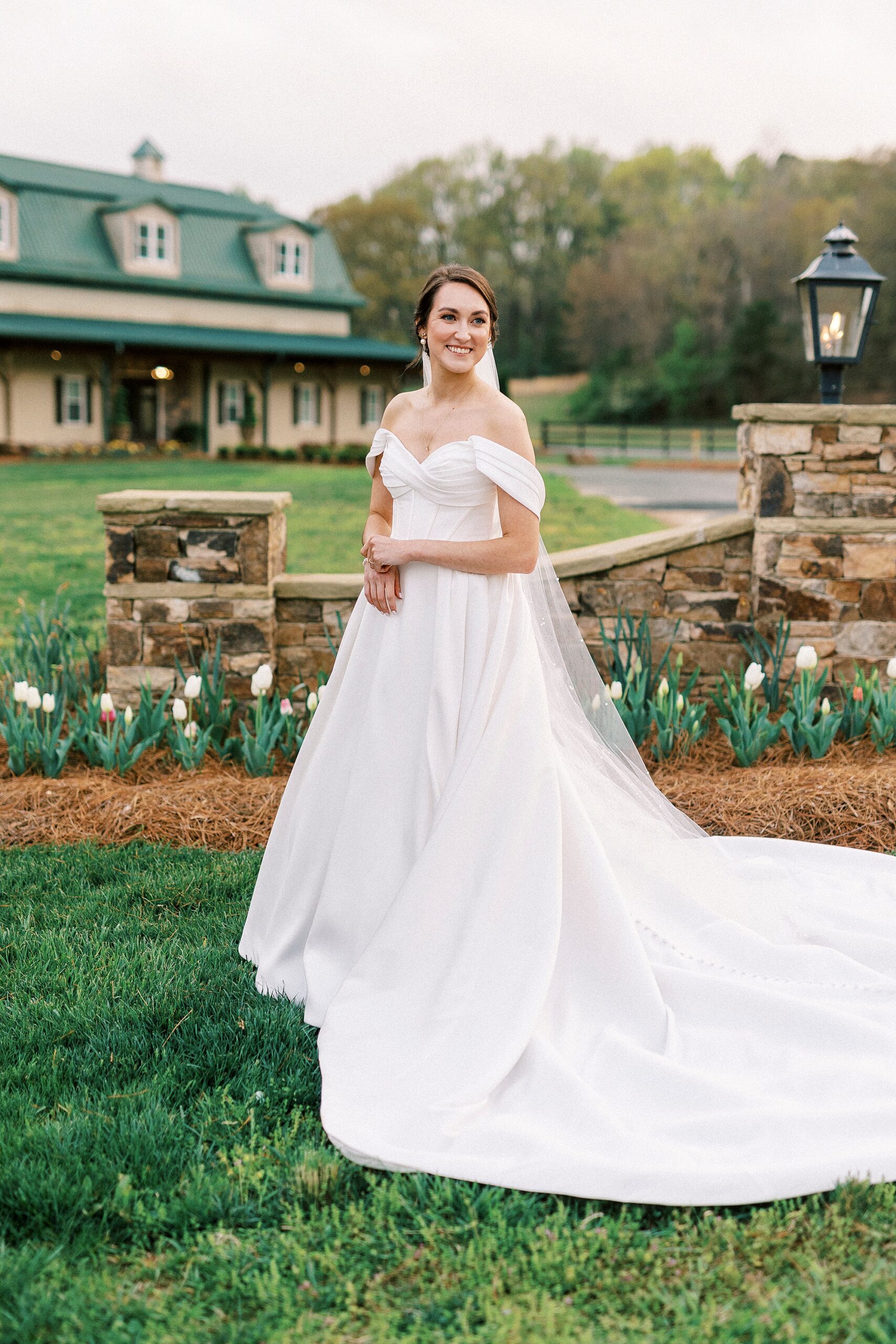 bride stands by stone wall on lawn at Low Meadows Estate