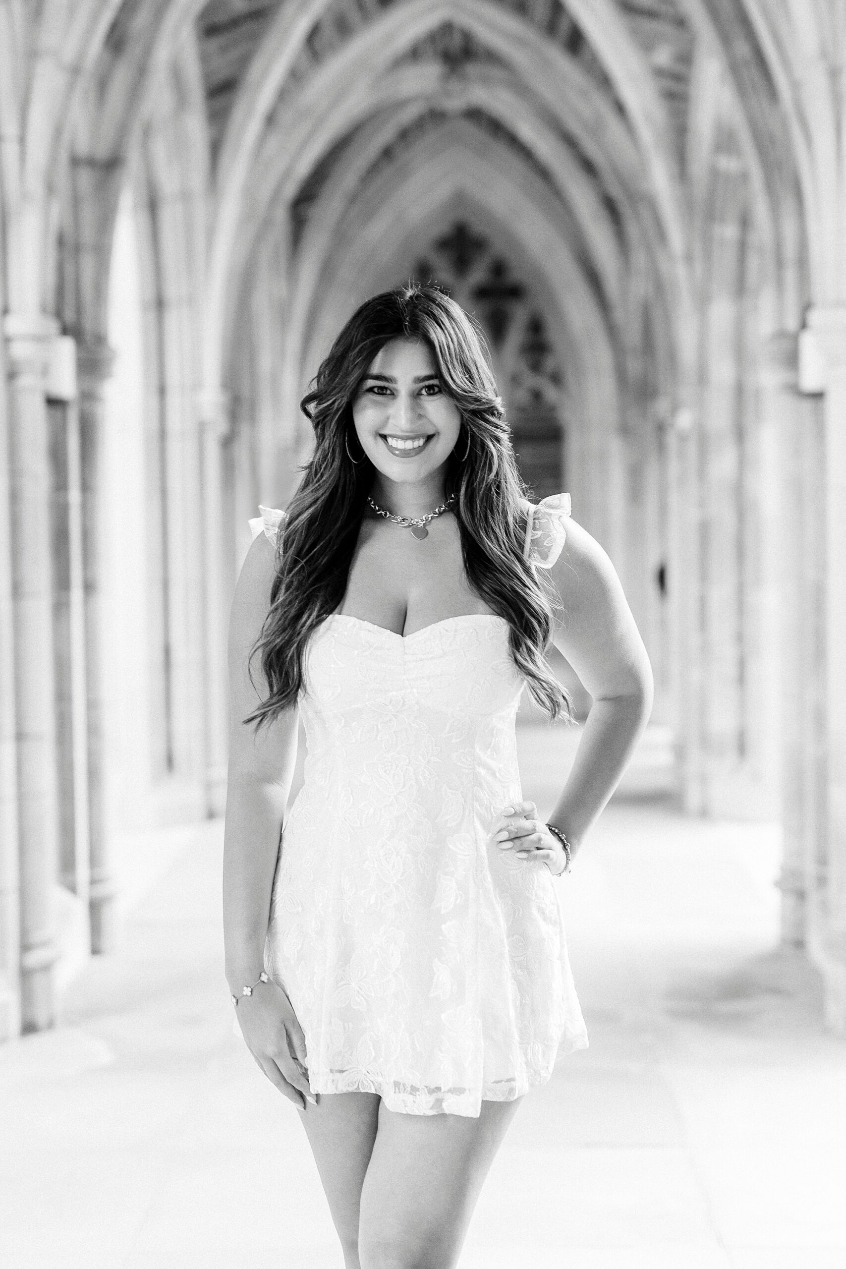 girl poses in white dress with hand on hip during Duke Chapel graduation portraits
