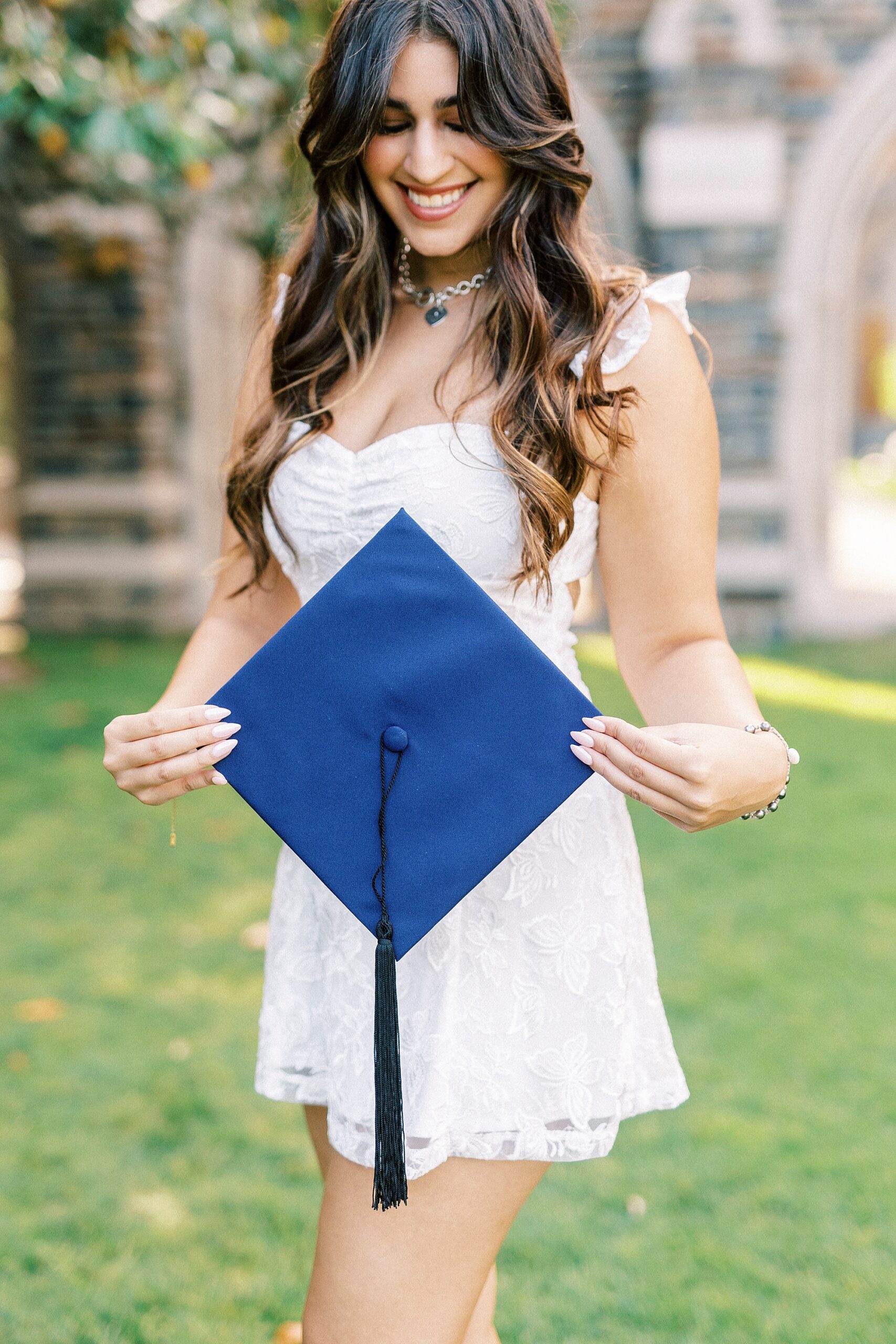 girl in white dress holds blue graduation cap