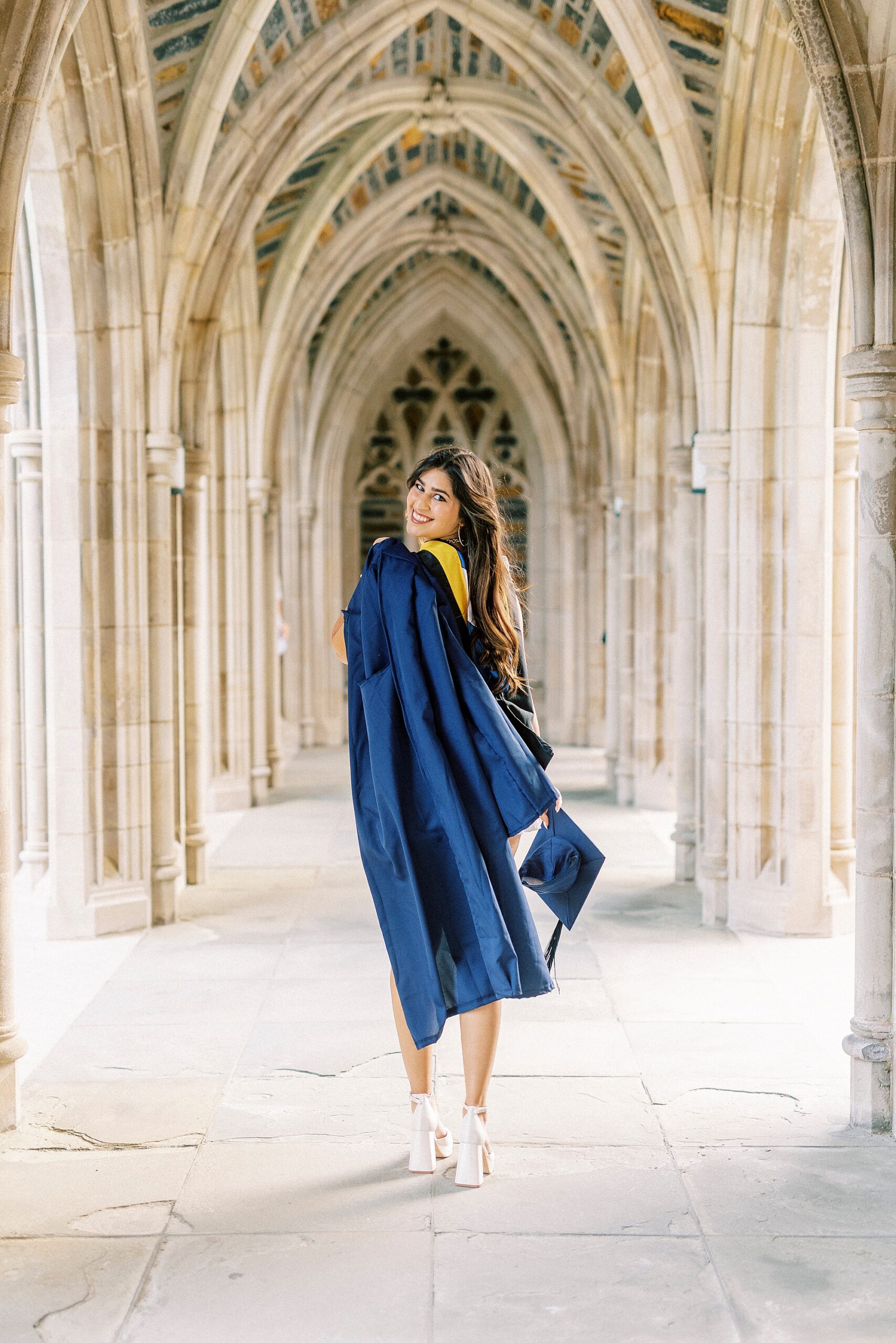senior walks down arches at Duke Chapel with graduation gown over her shoulder